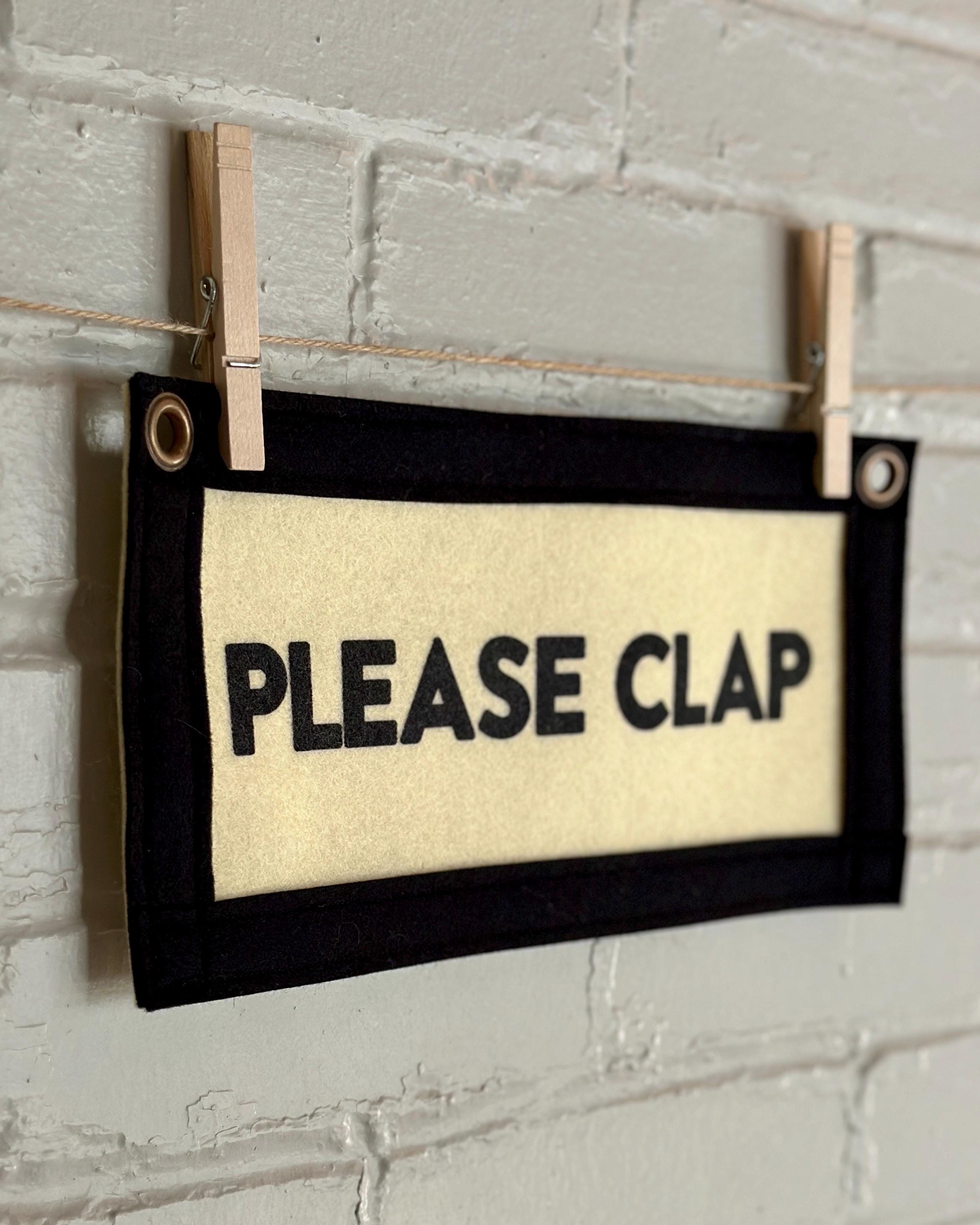 Side of a cream felt banner with black trim and lettering that reads "PLEASE CLAP"