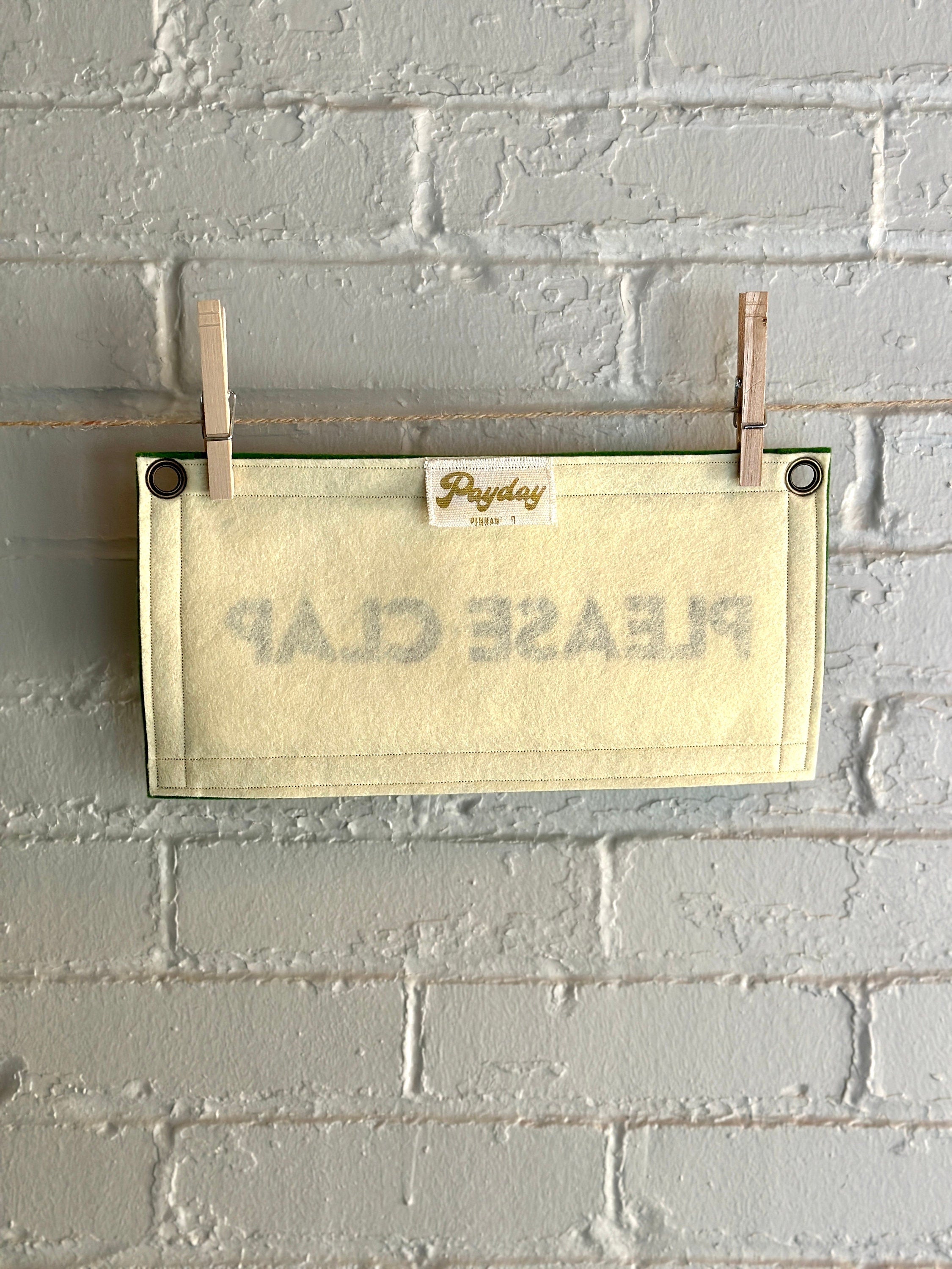 Back of cream felt banner with green trim and black lettering that reads "PLEASE CLAP"