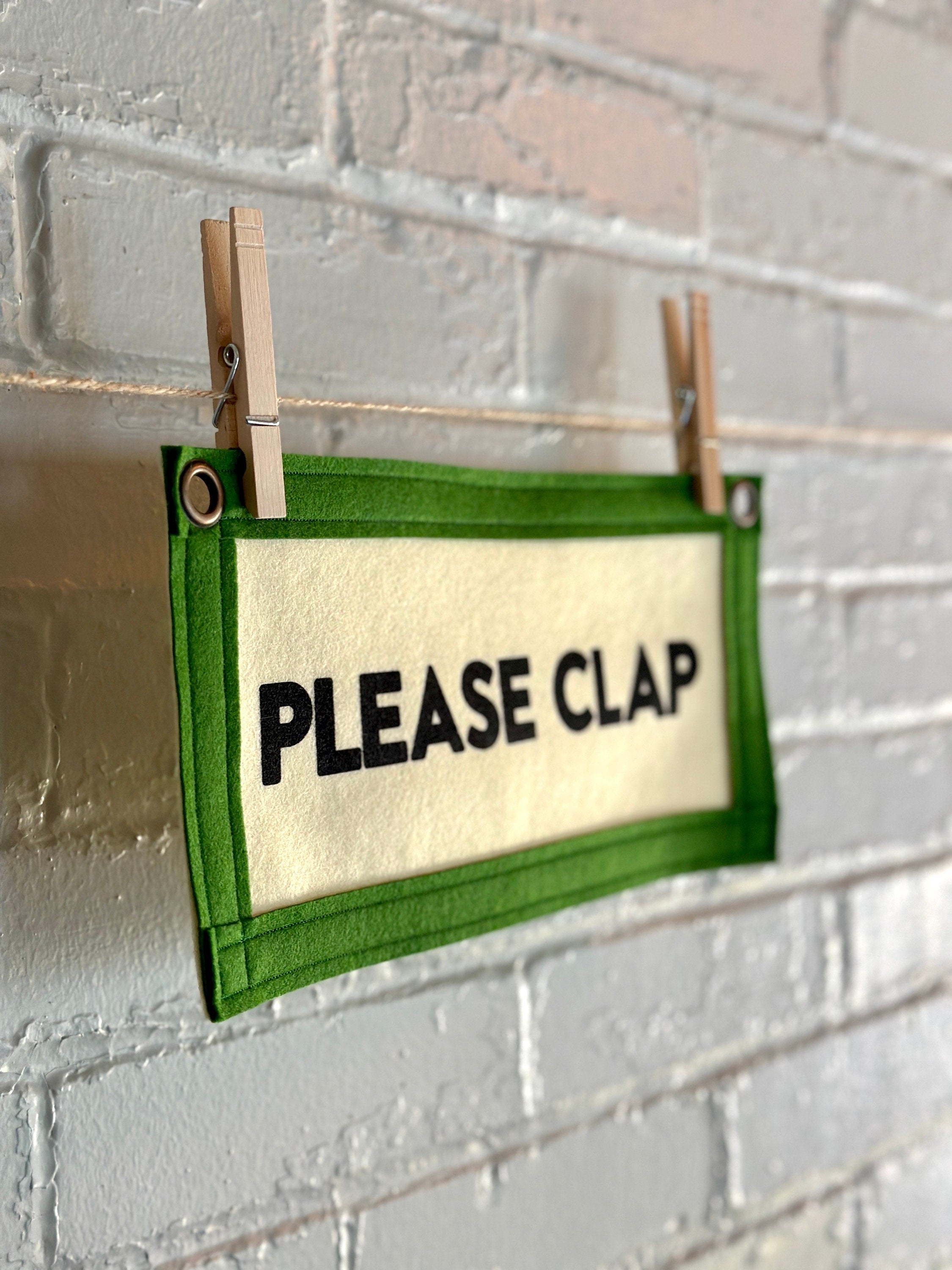 Side of a cream felt banner with green trim and black lettering that reads "PLEASE CLAP"