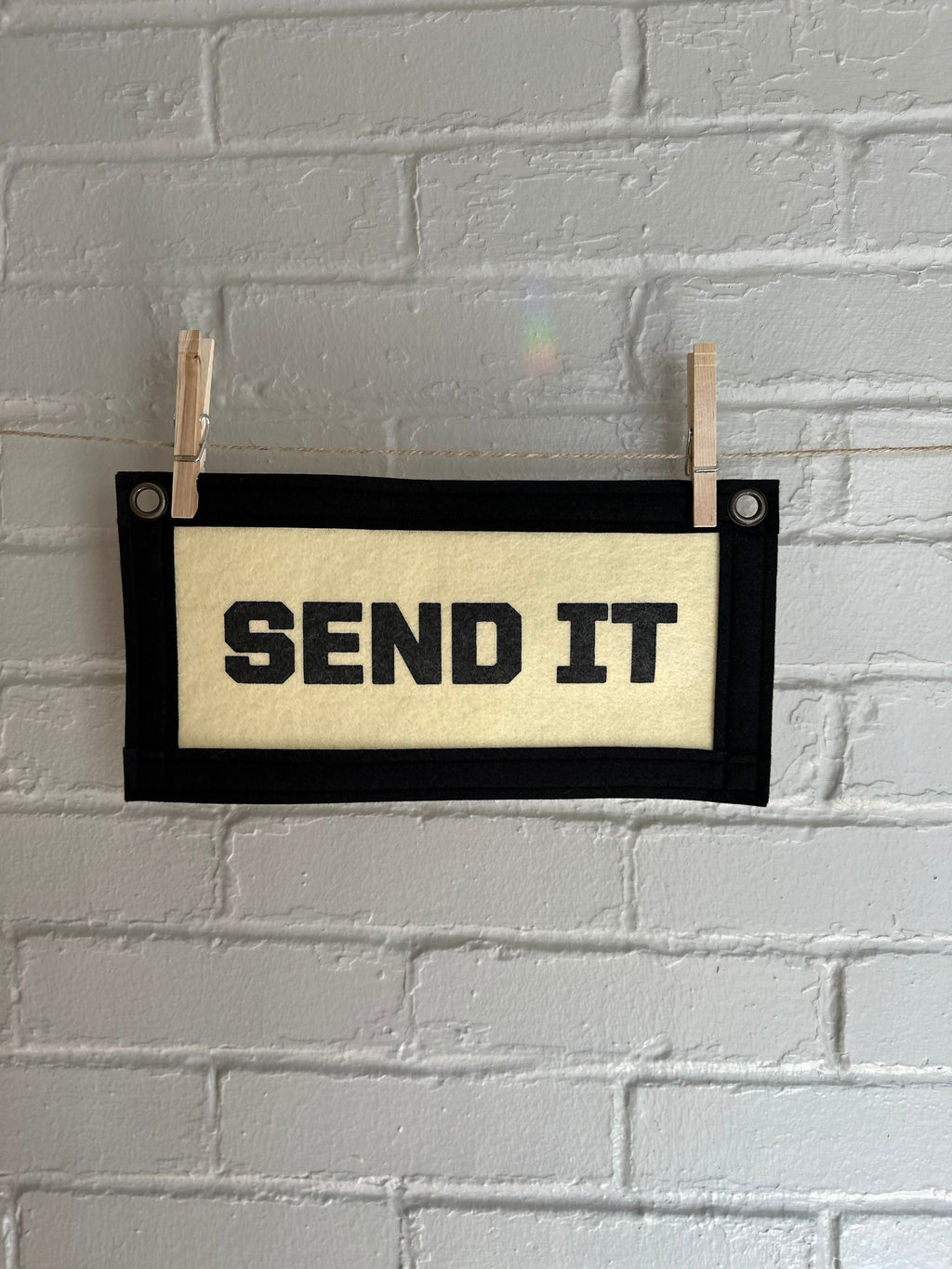 Cream felt banner with black trim and lettering that reads "SEND IT"