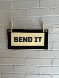 Cream felt banner with black trim and lettering that reads "SEND IT"