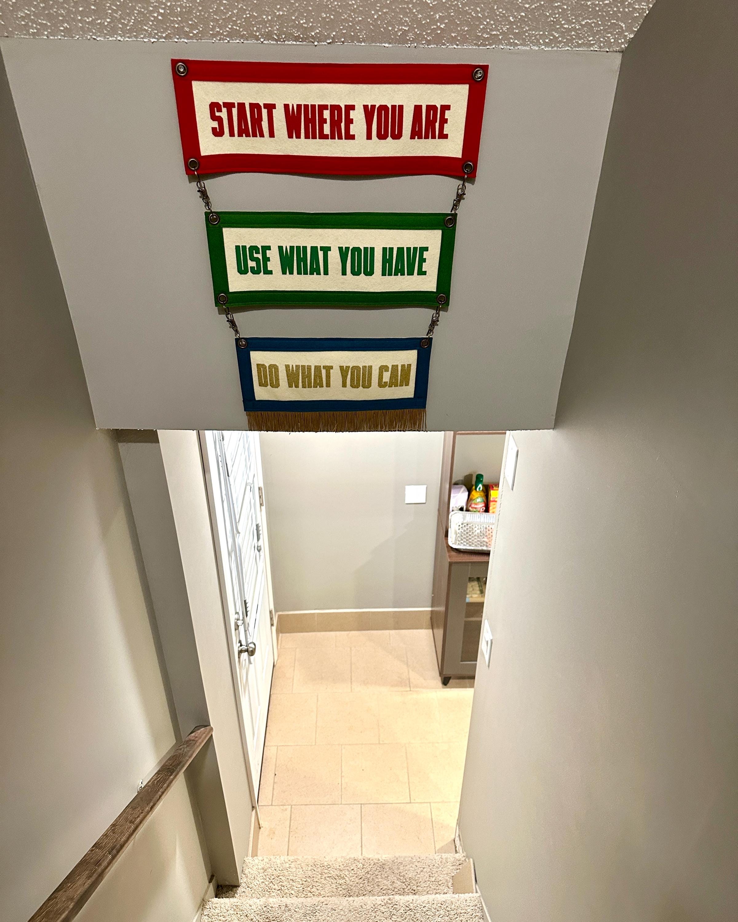 A stairwell with an upper wall where three colorful felt banners with motivational phrases attached by brass rings are hung