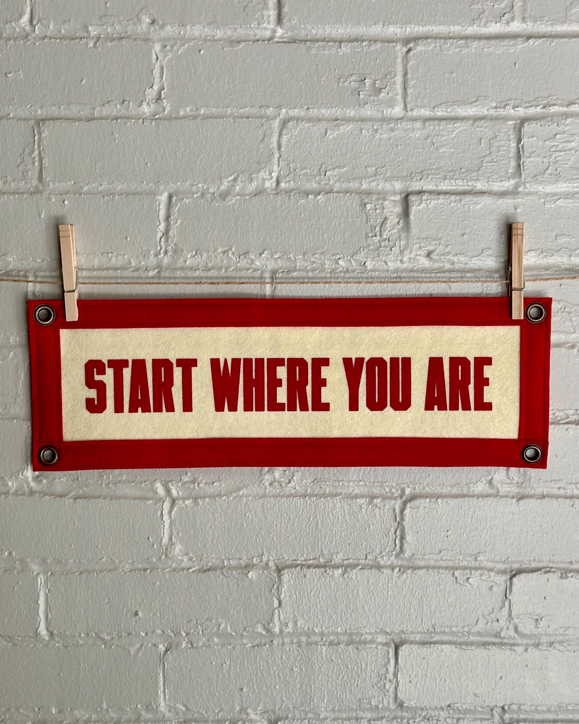 A cream felt banner with red trim and lettering that reads "Start where you are"