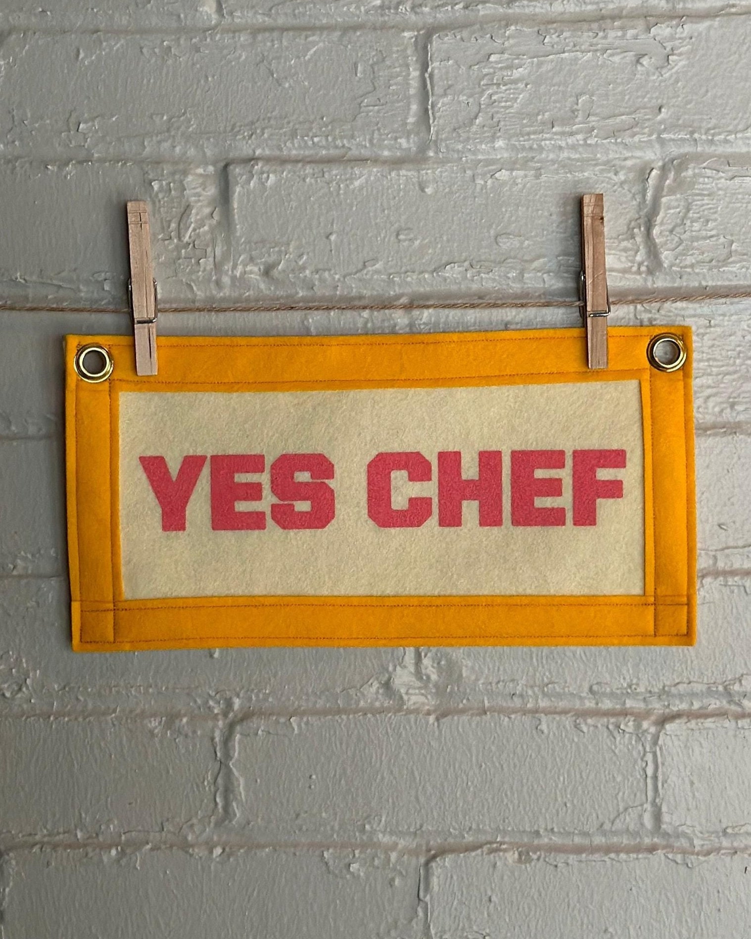 A cream felt banner with yellow trim and pink print reading "YES CHEF"