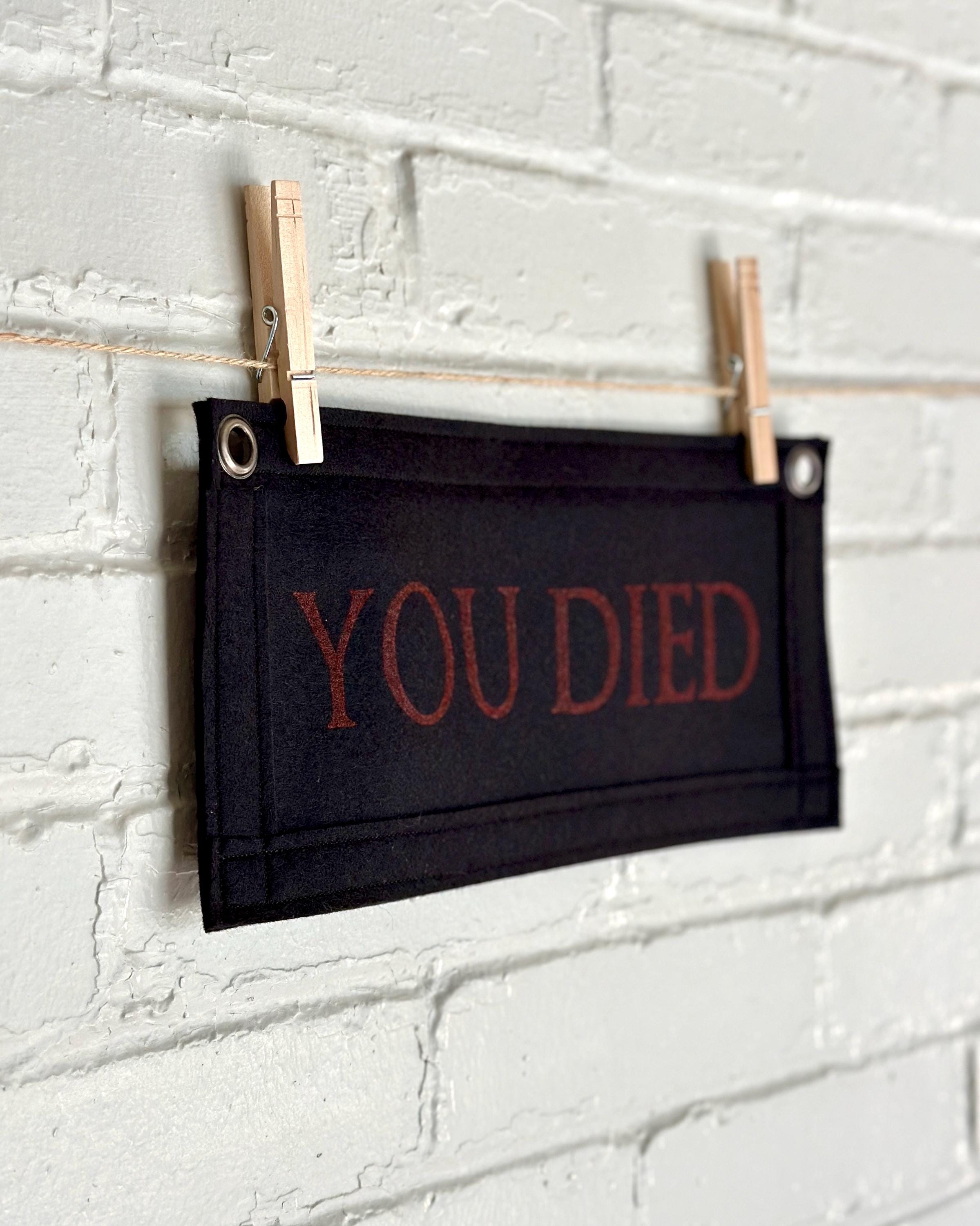 Side view of a black felt banner with black trim and red lettering that reads 'YOU DIED'