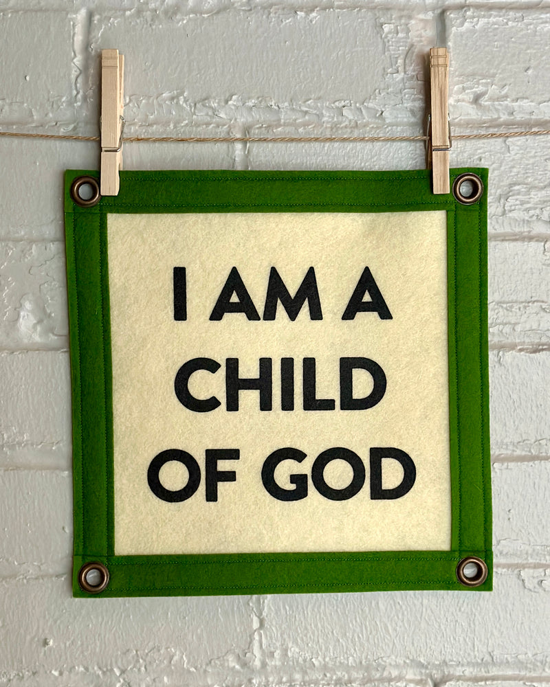 A square shaped cream felt banner with green trim and the phrase "I am a child of god" printed in black ink