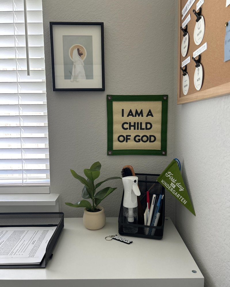 A desk and the wall behind it with art including a felt banner reading "I am a child of god"