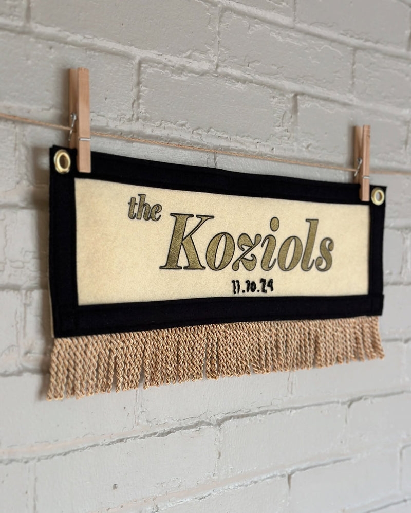 Cream banner with black trim and gold fringe, with 'the Koziols' printed in gold ink
