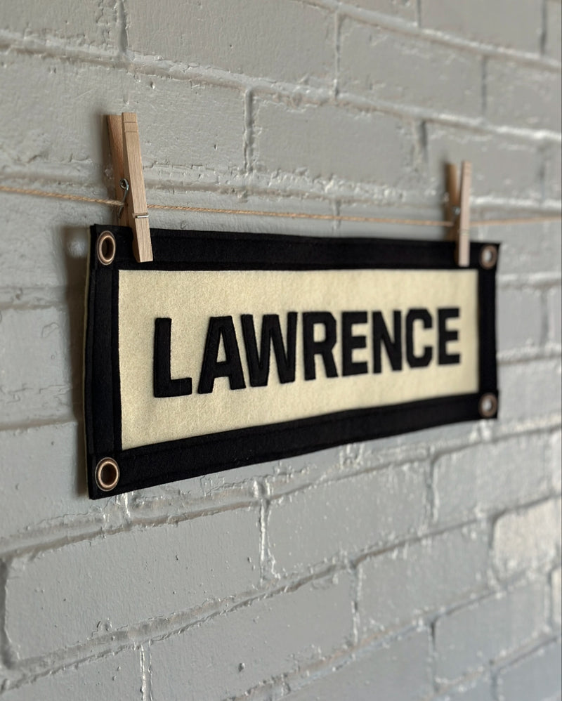Cream banner with black trim and black sewn letters spelling 'LAWRENCE' 