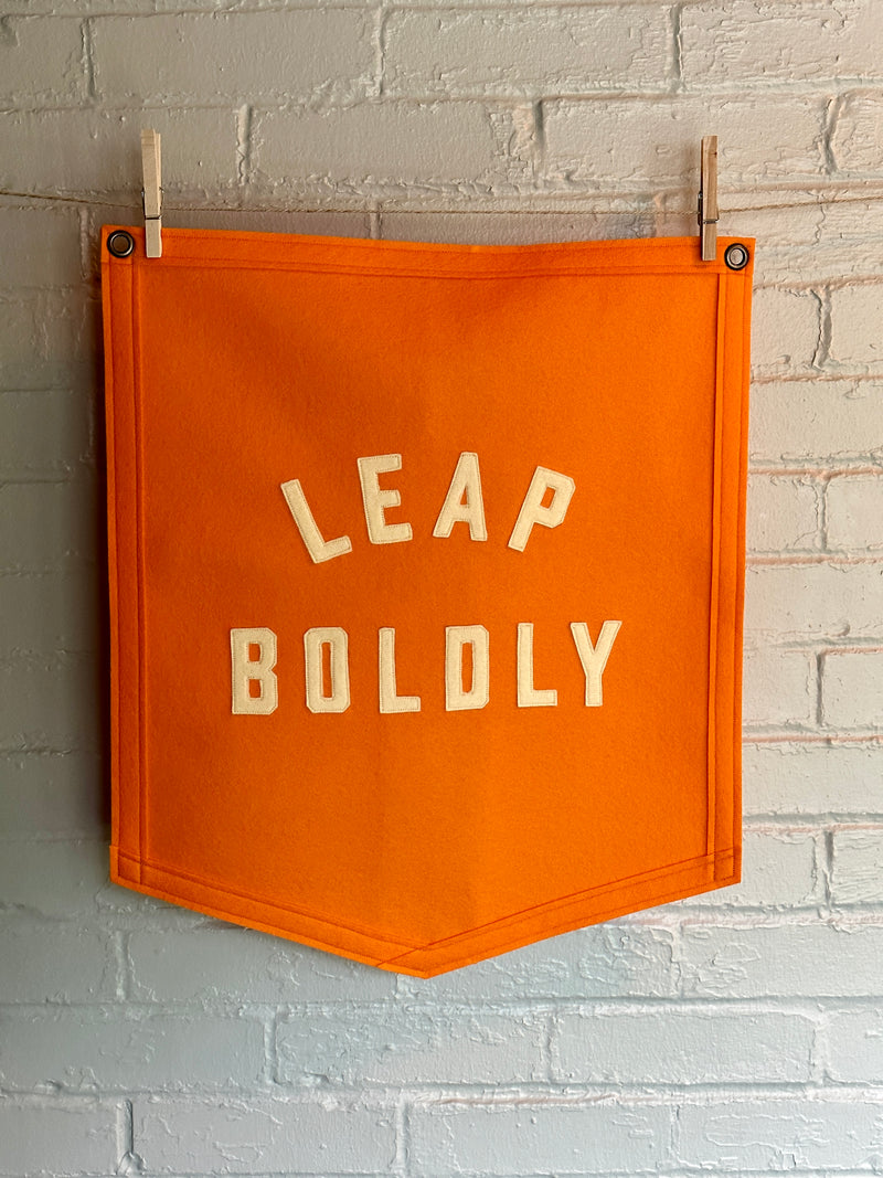 Orange banner with 'LEAP BOLDLY' text hanging on a brick wall