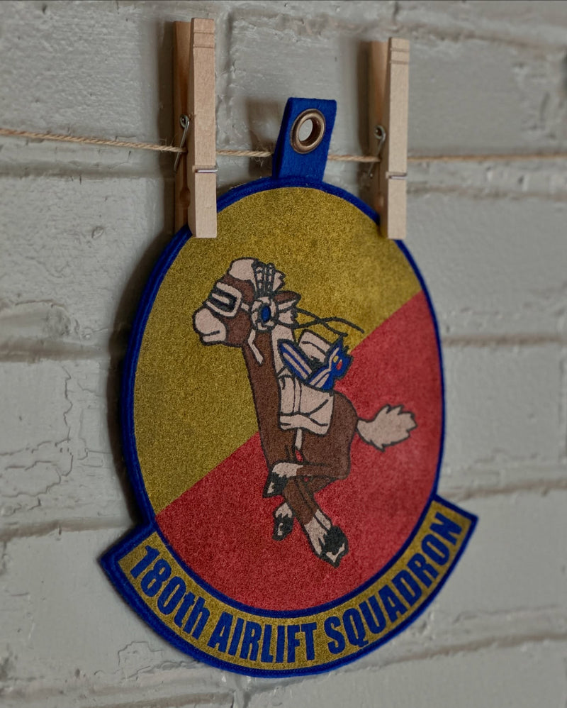 Patch of the 180th Airlift Squadron with a camel design on a white brick wall.