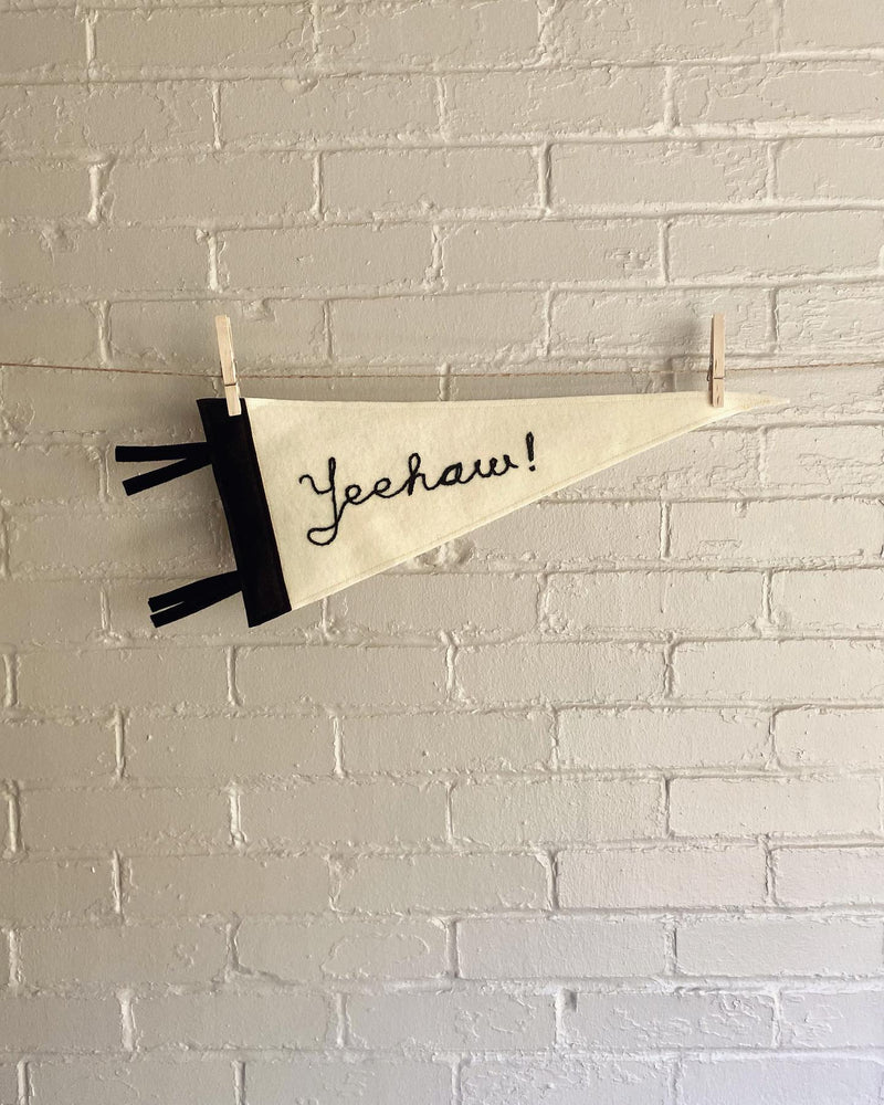 A black and cream pennant with the word "Yeehaw!" chain stitched on it 