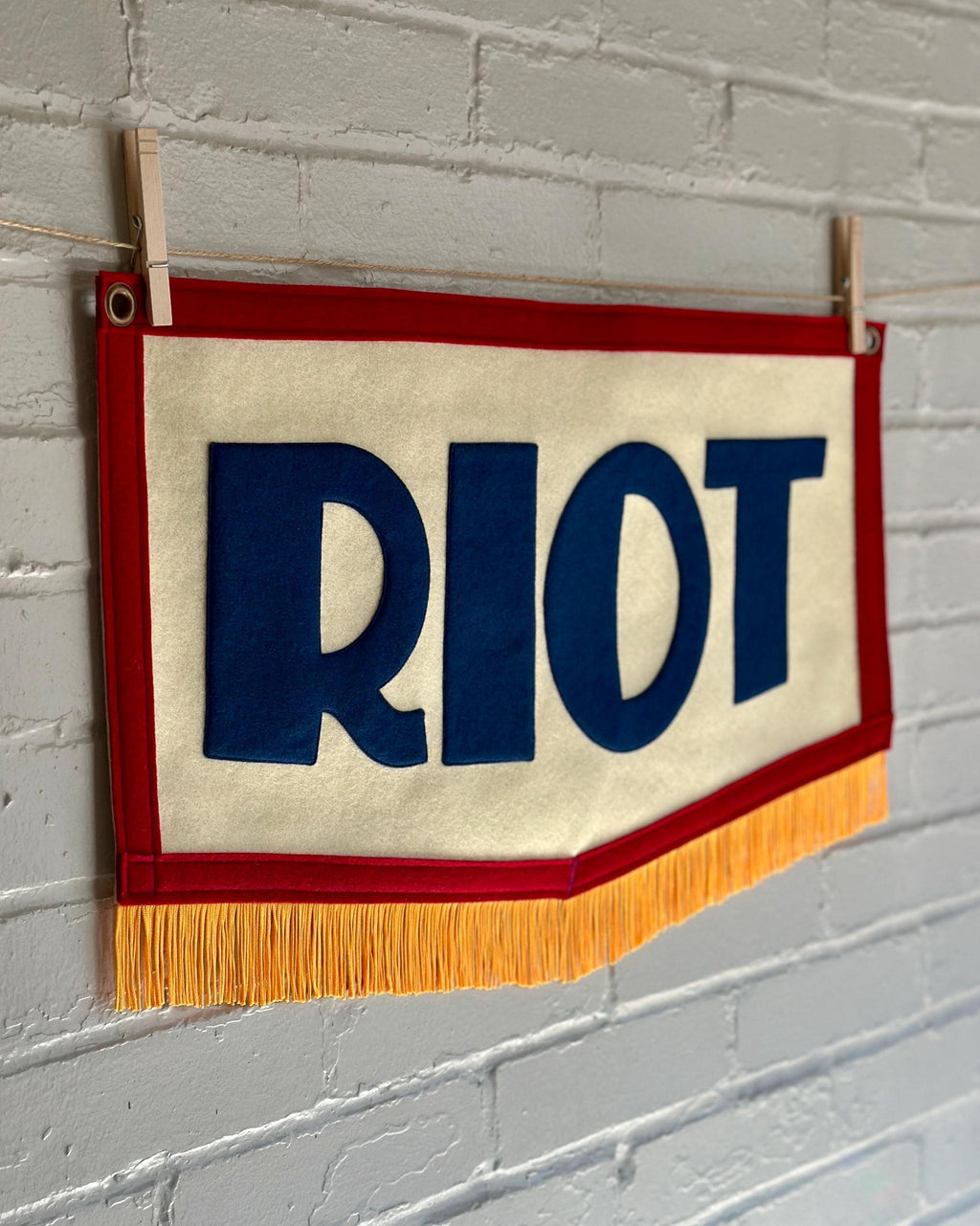 A red, white and blue felt banner with flag gold trim and appliqué letters that read RIOT