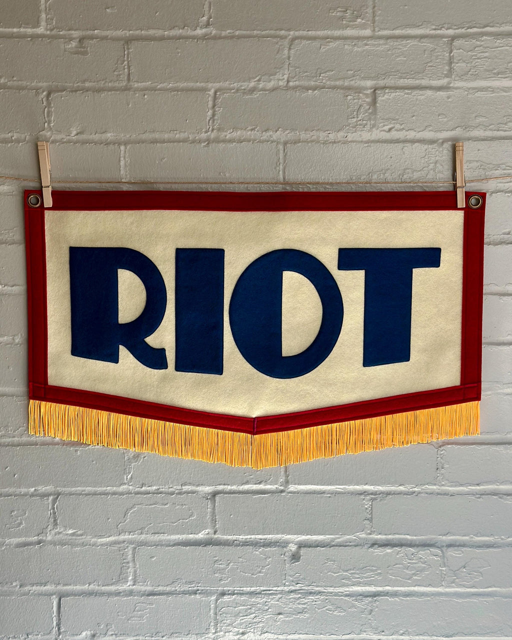 A red, white and blue felt banner with flag gold trim and appliqué letters that read RIOT