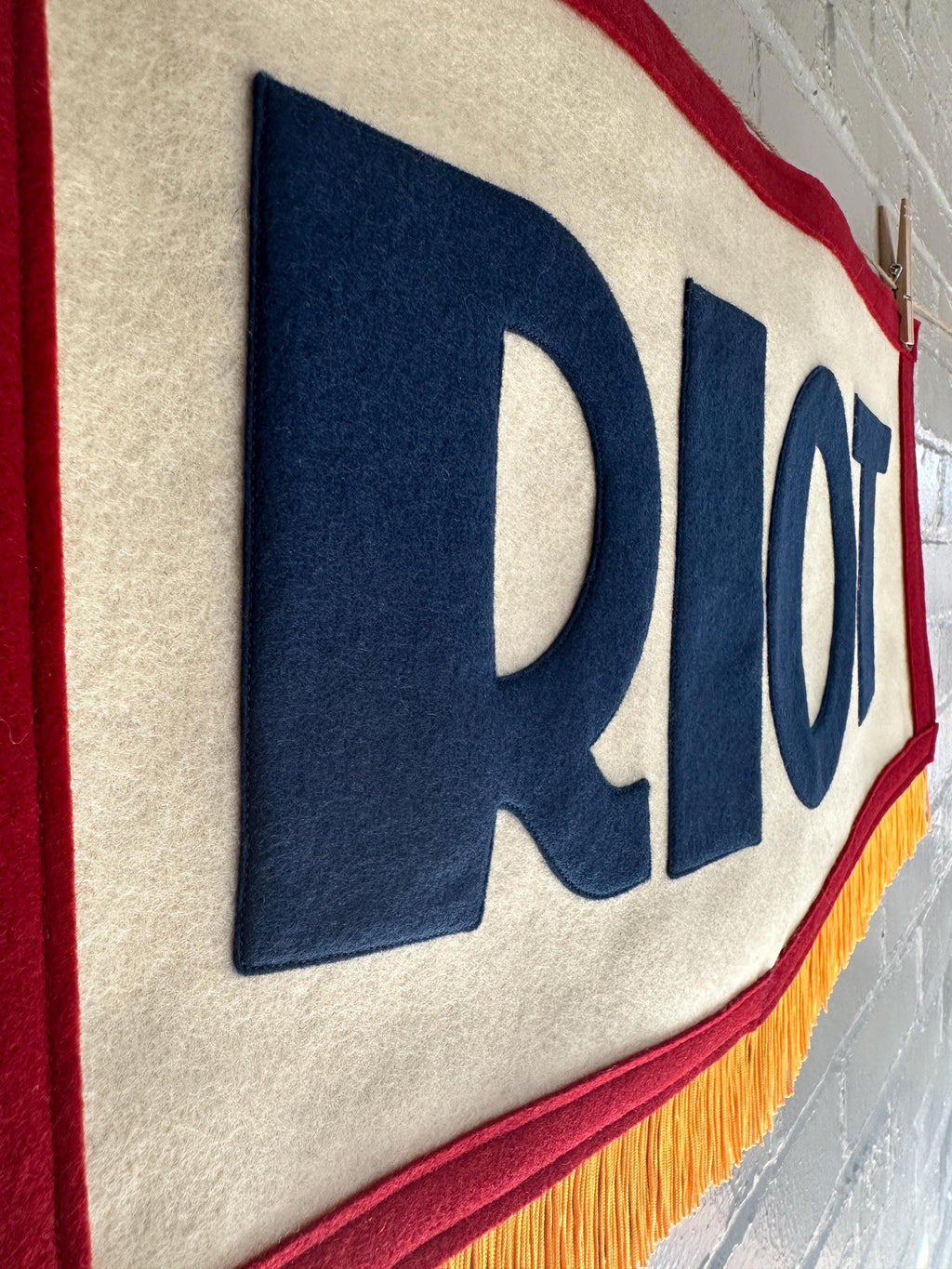 A red, white and blue felt banner with flag gold trim and appliqué letters that read RIOT