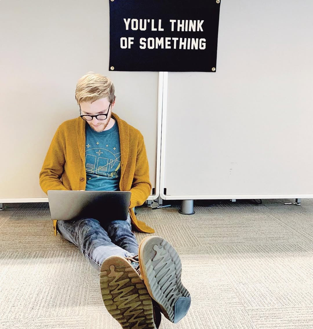 Person sitting on the floor using a laptop with an Oxford Pennant banner that reads "YOU'LL THINK OF SOMETHING" above them.