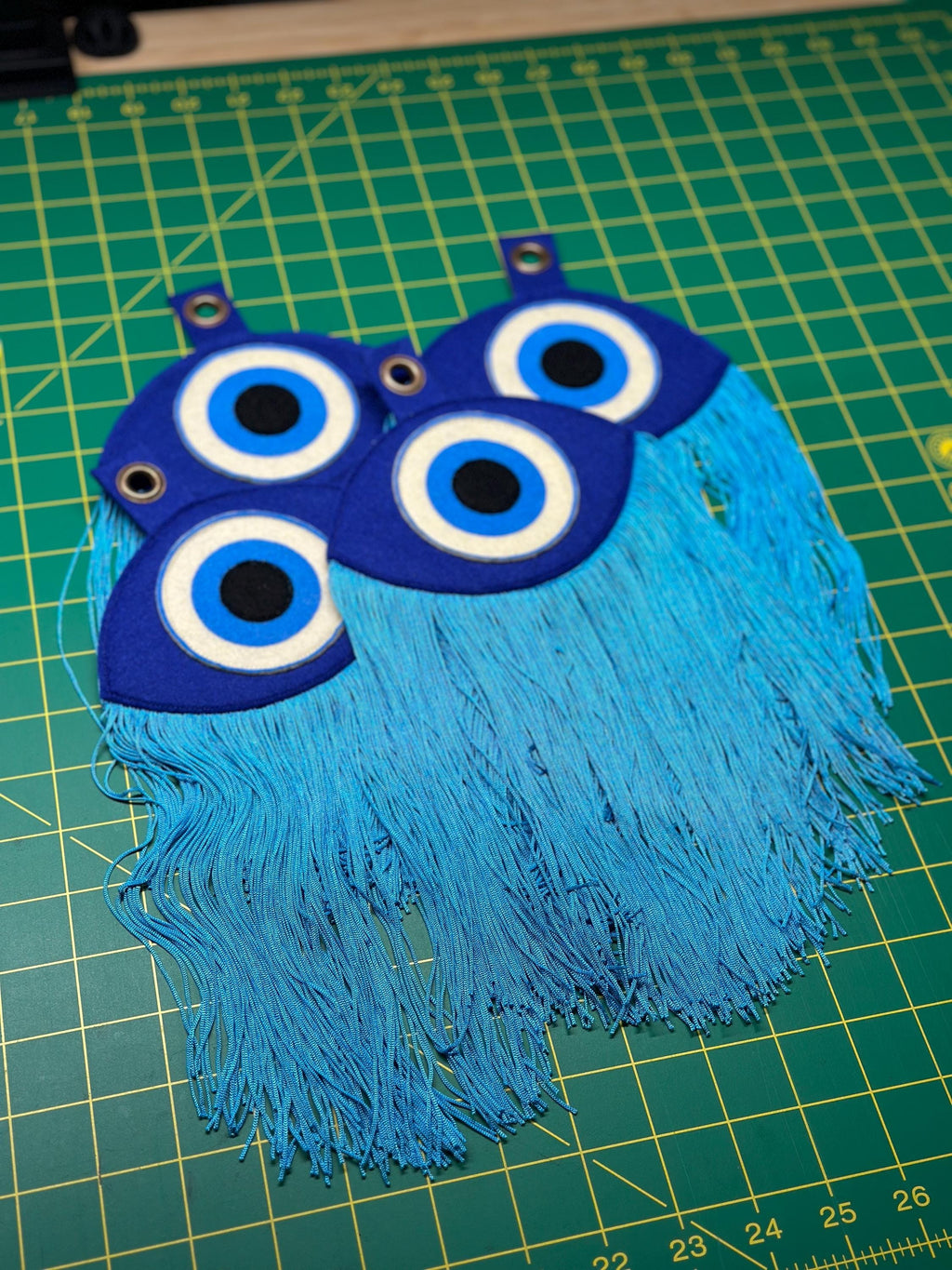 Multiple "evil eye" felt creations displayed on a cutting mat