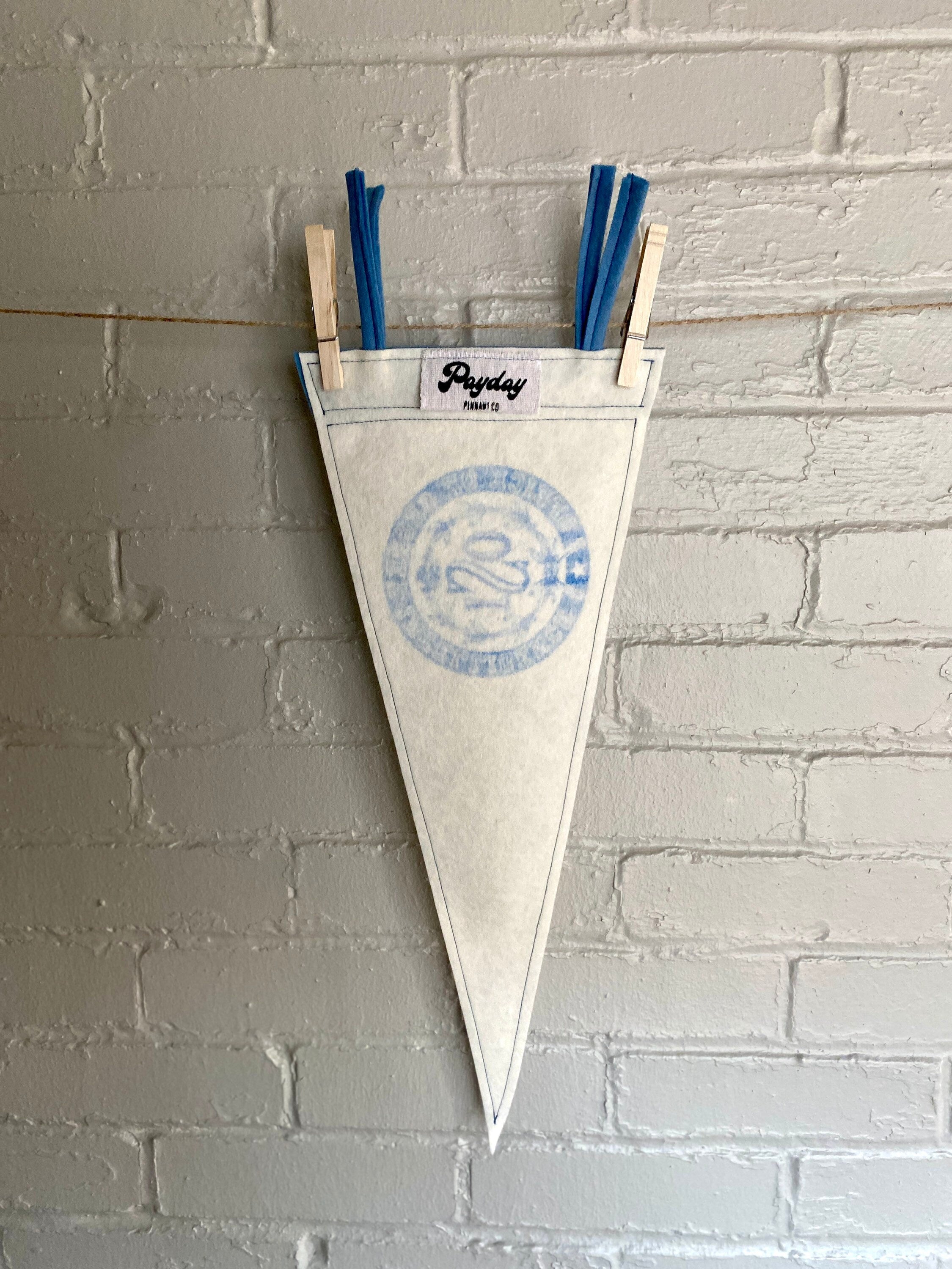 A white felt pennant with light blue trim and the OSI logo from the cartoon The Venture Bros printed in blue ink