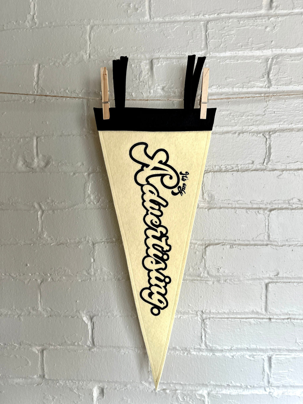 A cream pennant with black trim and print that reads "It's just advertising"