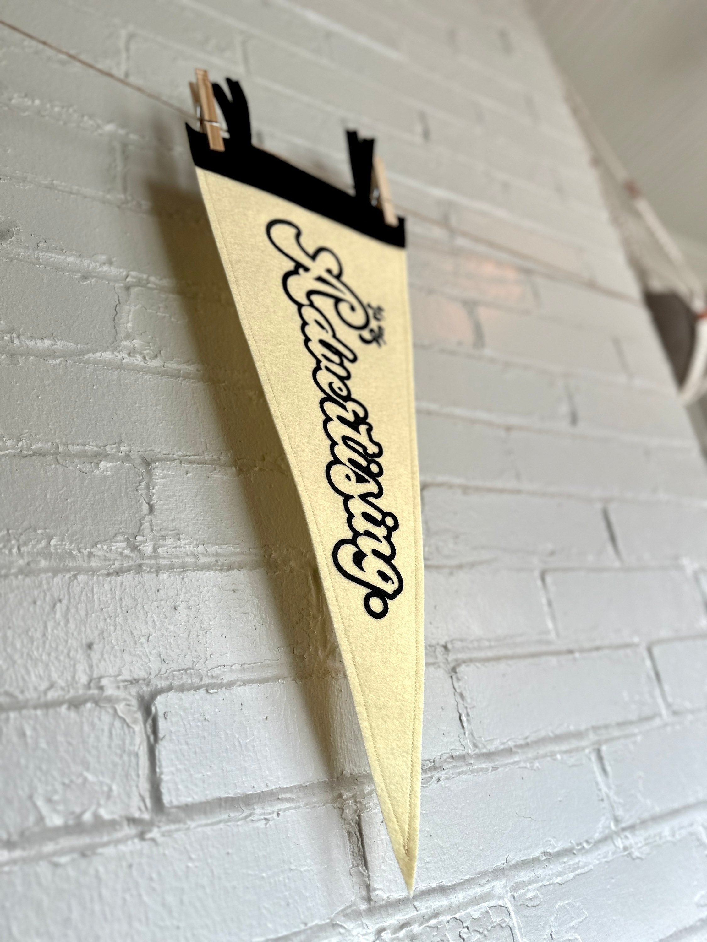 The side, back view of a cream felt pennant with black trim and print that reads "It's just advertising"