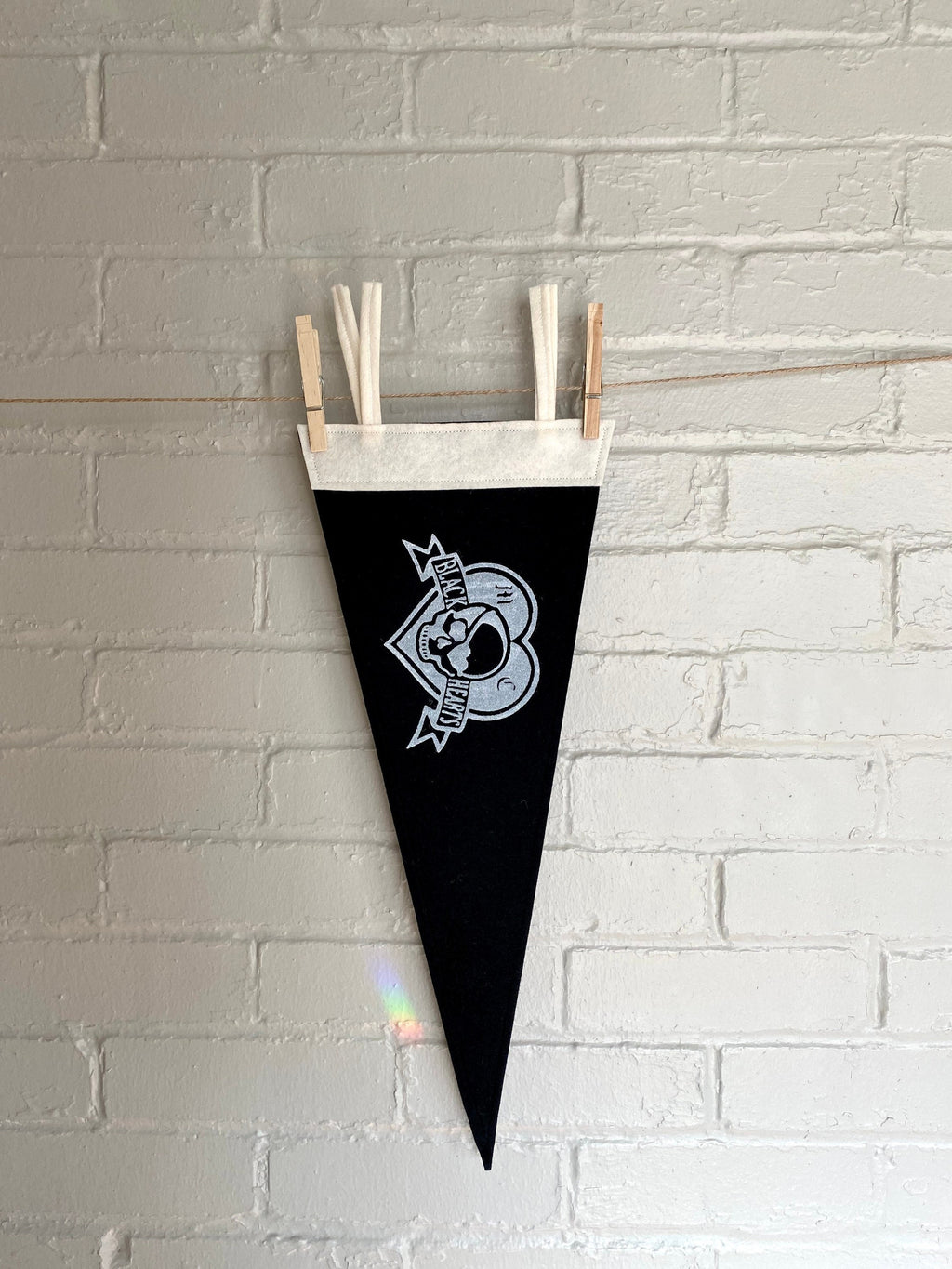 A black pennant hanging vertically, with white trim and the Venture Bros "Black Hearts" logo printed on