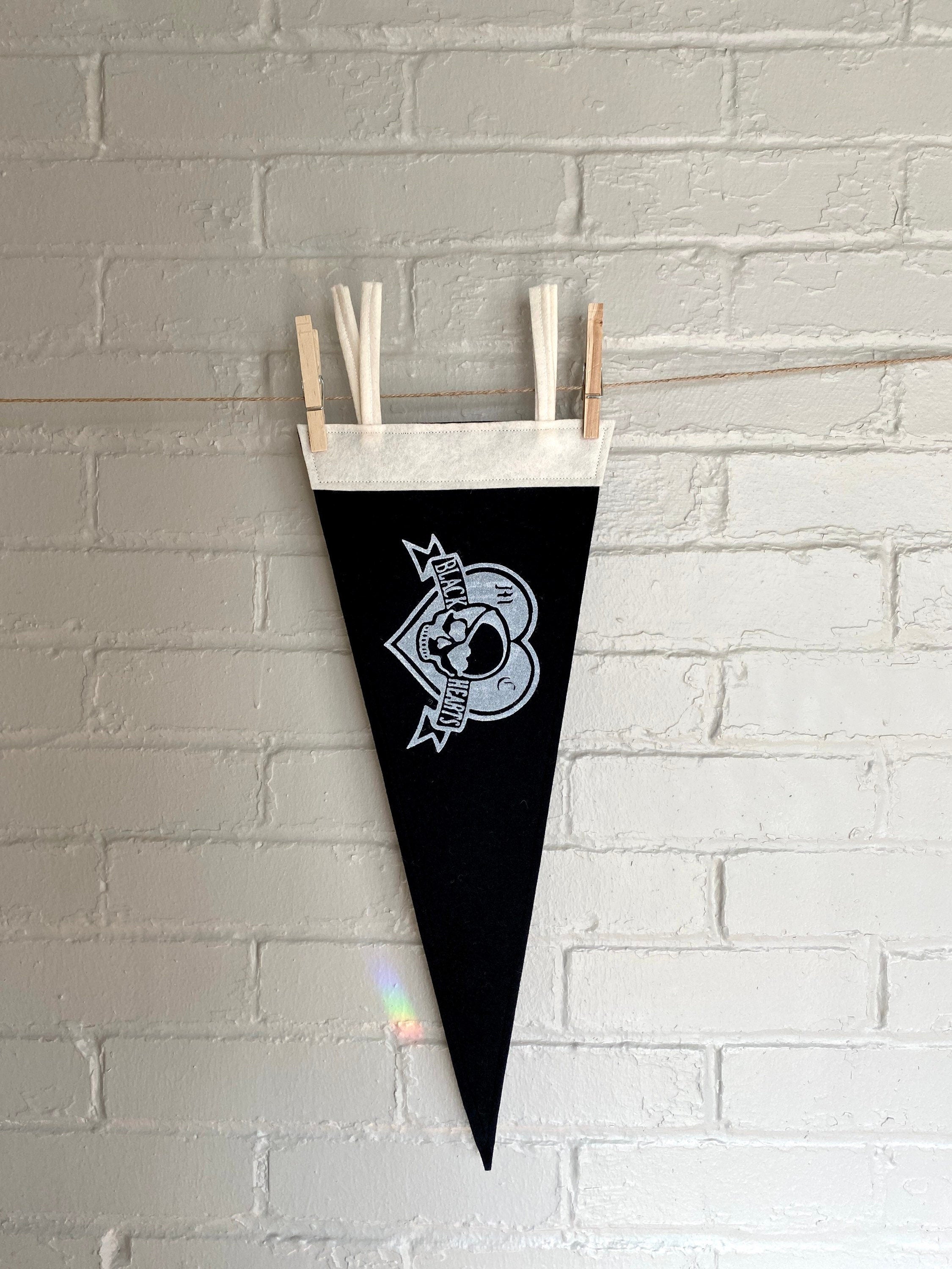 A black pennant hanging vertically, with white trim and the Venture Bros "Black Hearts" logo printed on