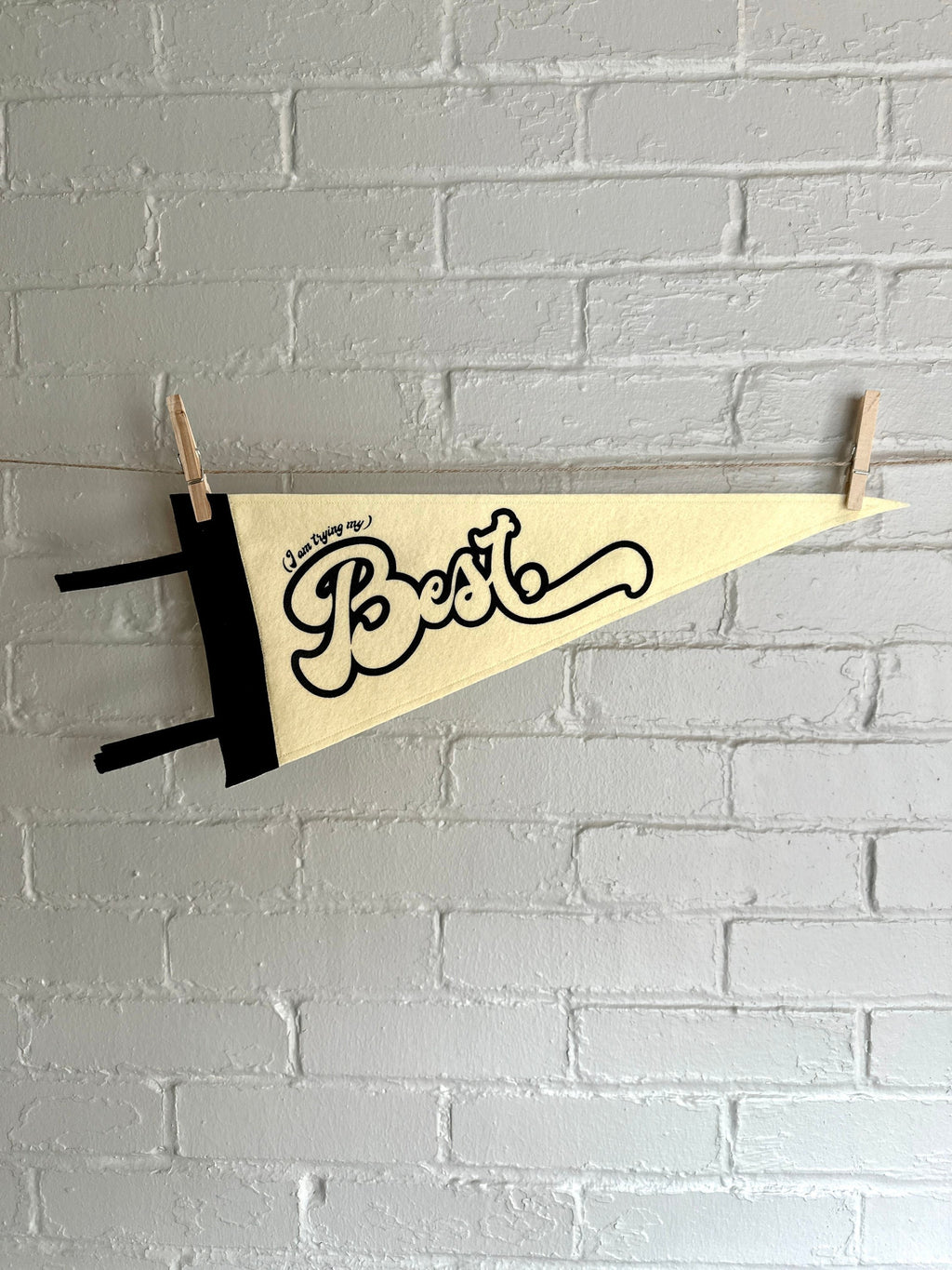 A cream felt pennant with black trim and black lettering that reads "I'm trying my best"