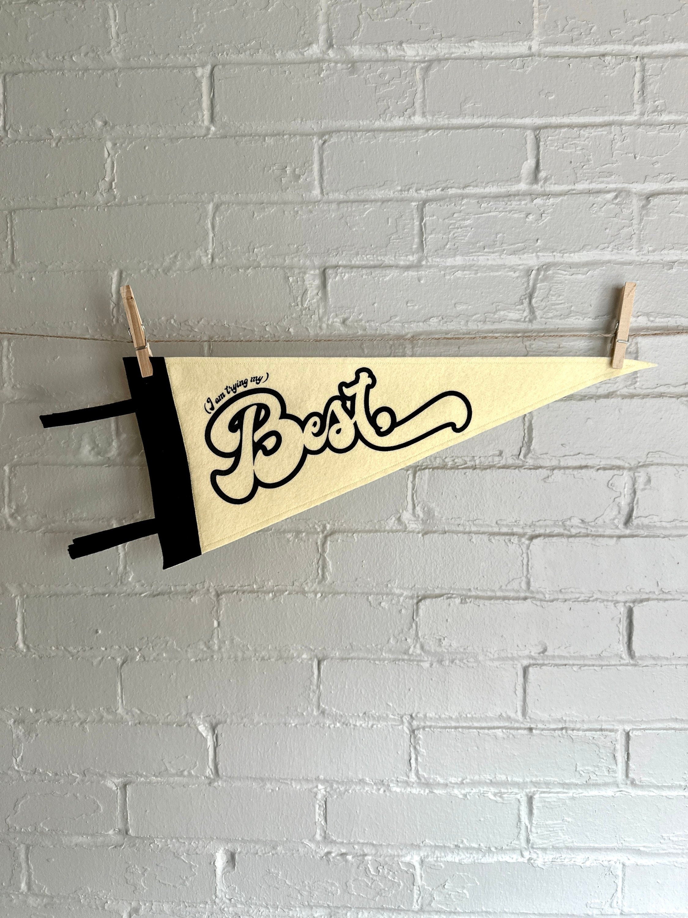 A cream felt pennant with black trim and black lettering that reads "I'm trying my best"