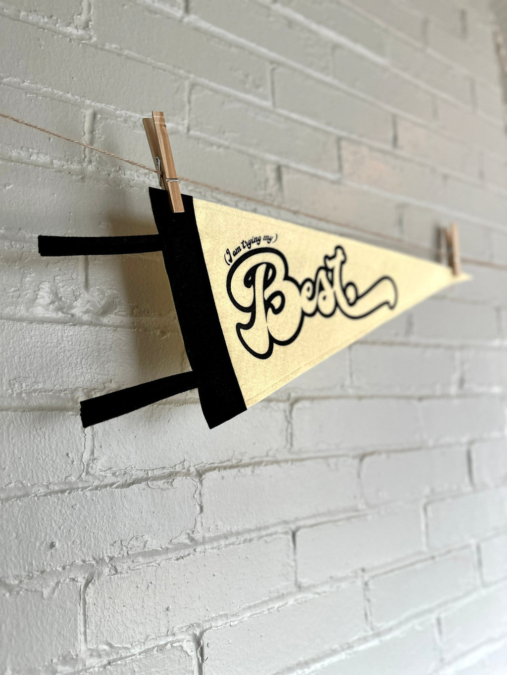 The side view of a cream felt pennant with black trim and black lettering that reads "I'm trying my best"