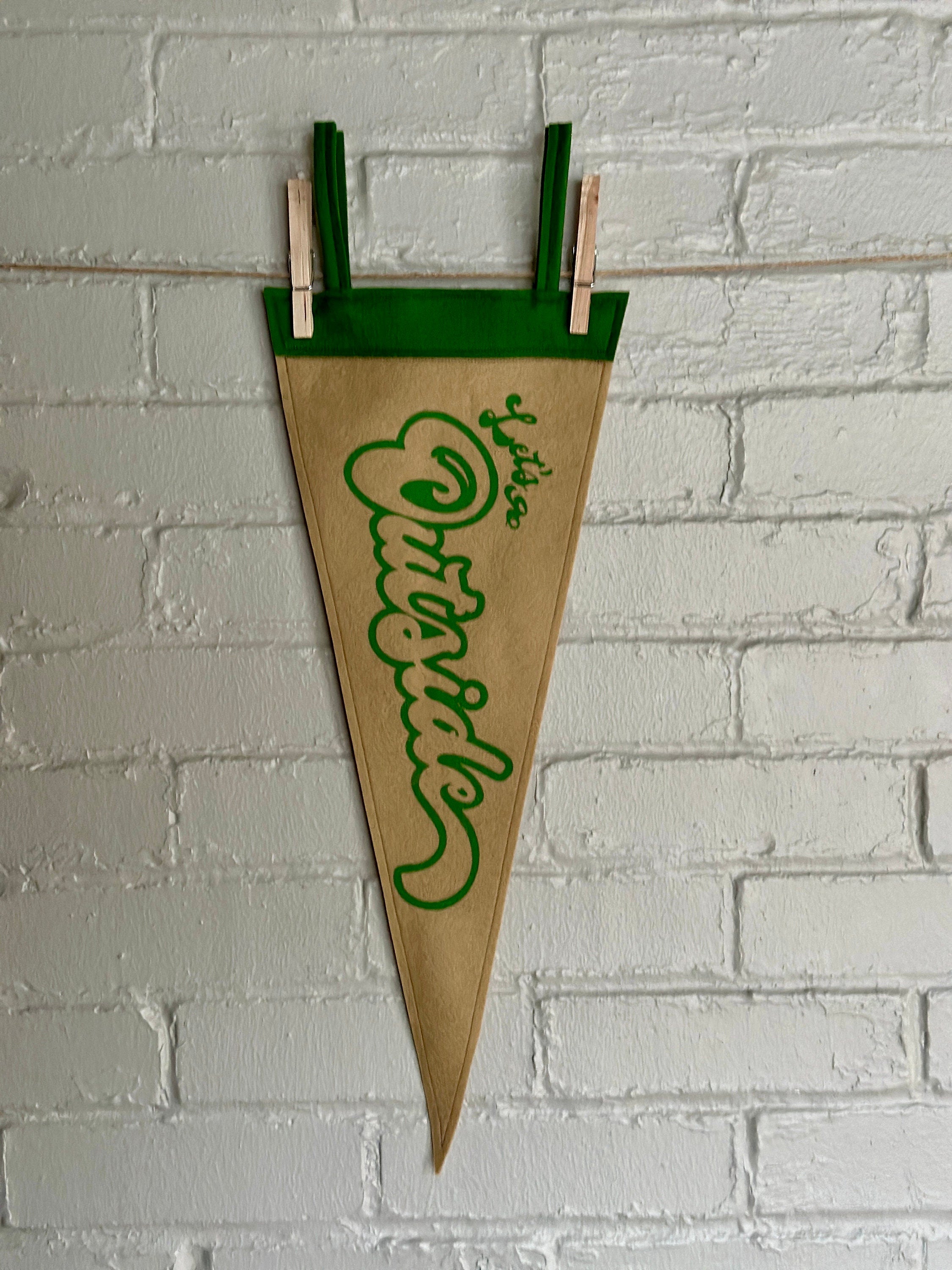 Light brown felt pennant with green trim and green flowy lettering that reads "Let's go outside"