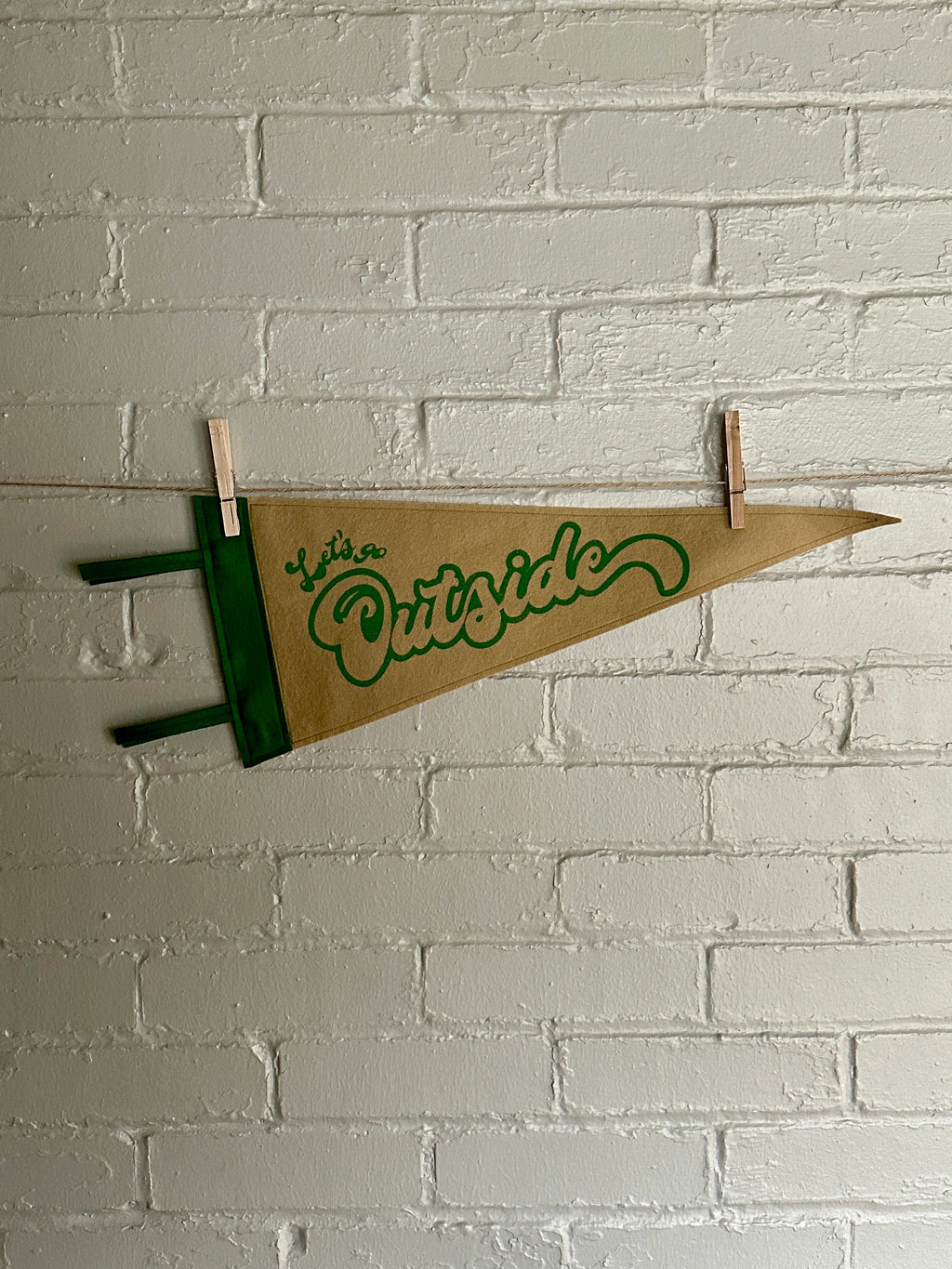 Light brown felt pennant with green trim and green flowy lettering that reads "Let's go outside"