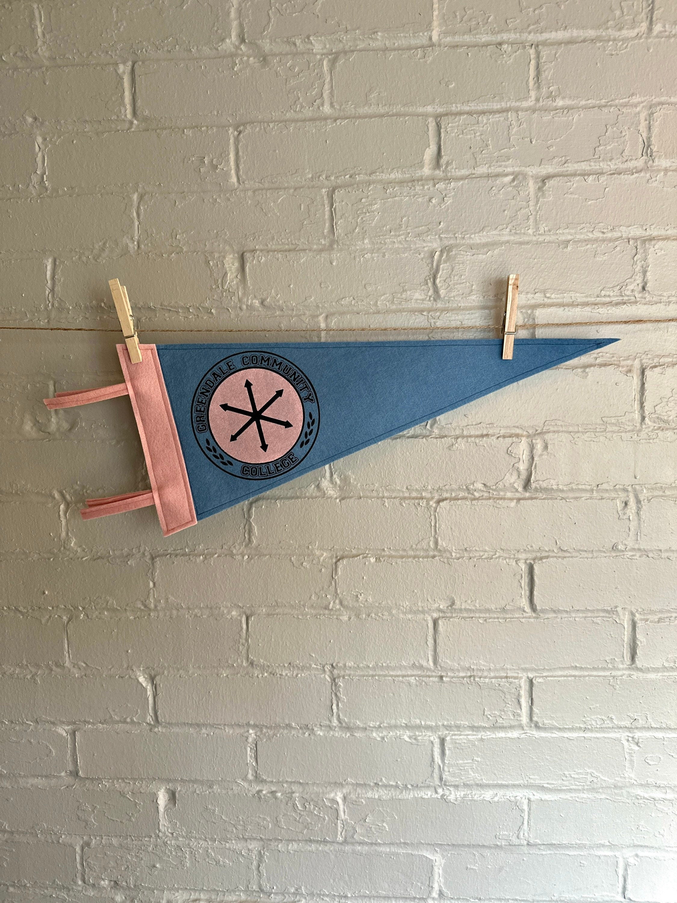 A light blue felt pennant with pink trim and a Greendale Community College logo printed on