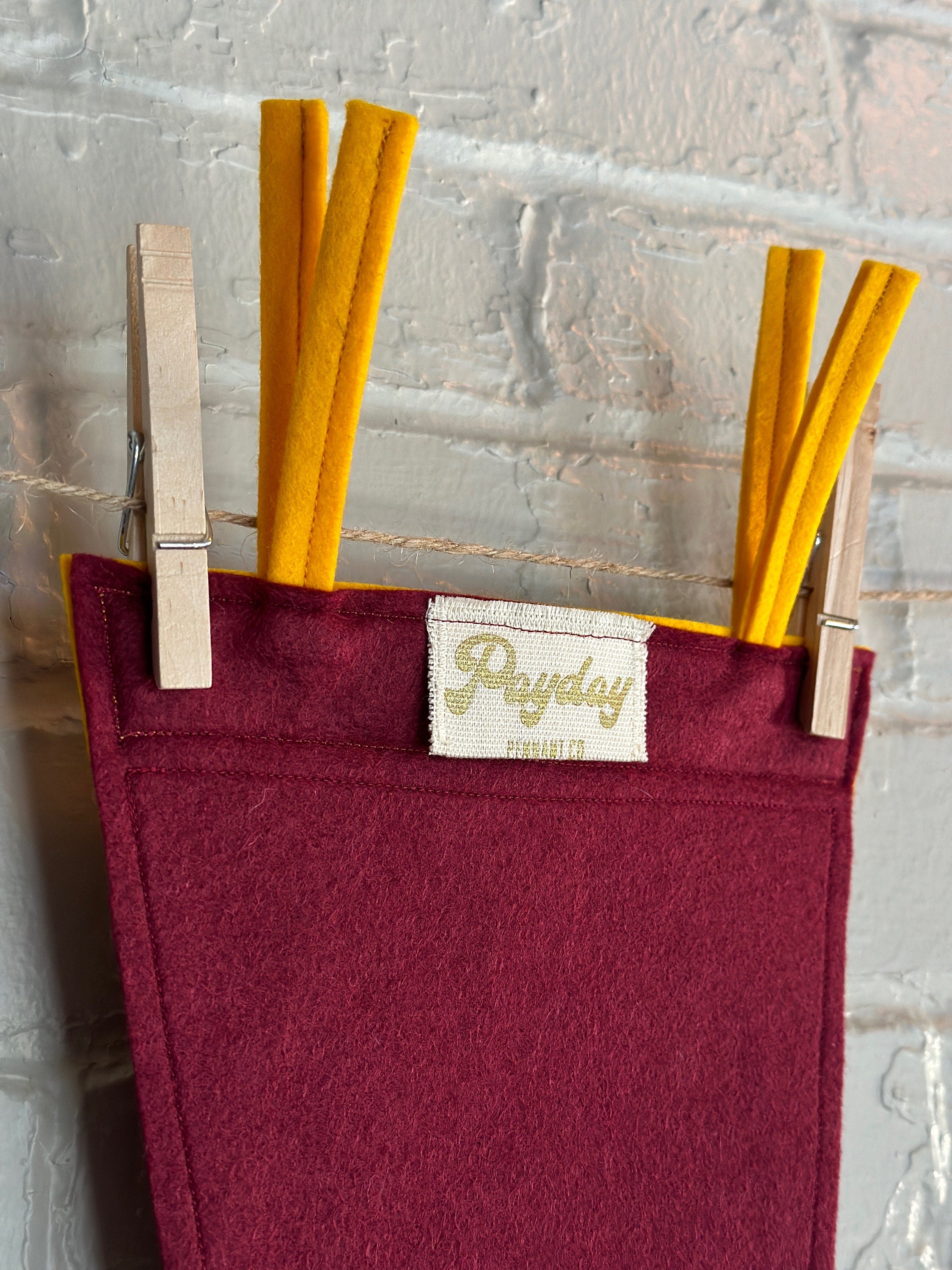 Closeup of the back of a burgundy pennant with yellow felt trim and the Guild of Calamitous Intent logo printed in gold