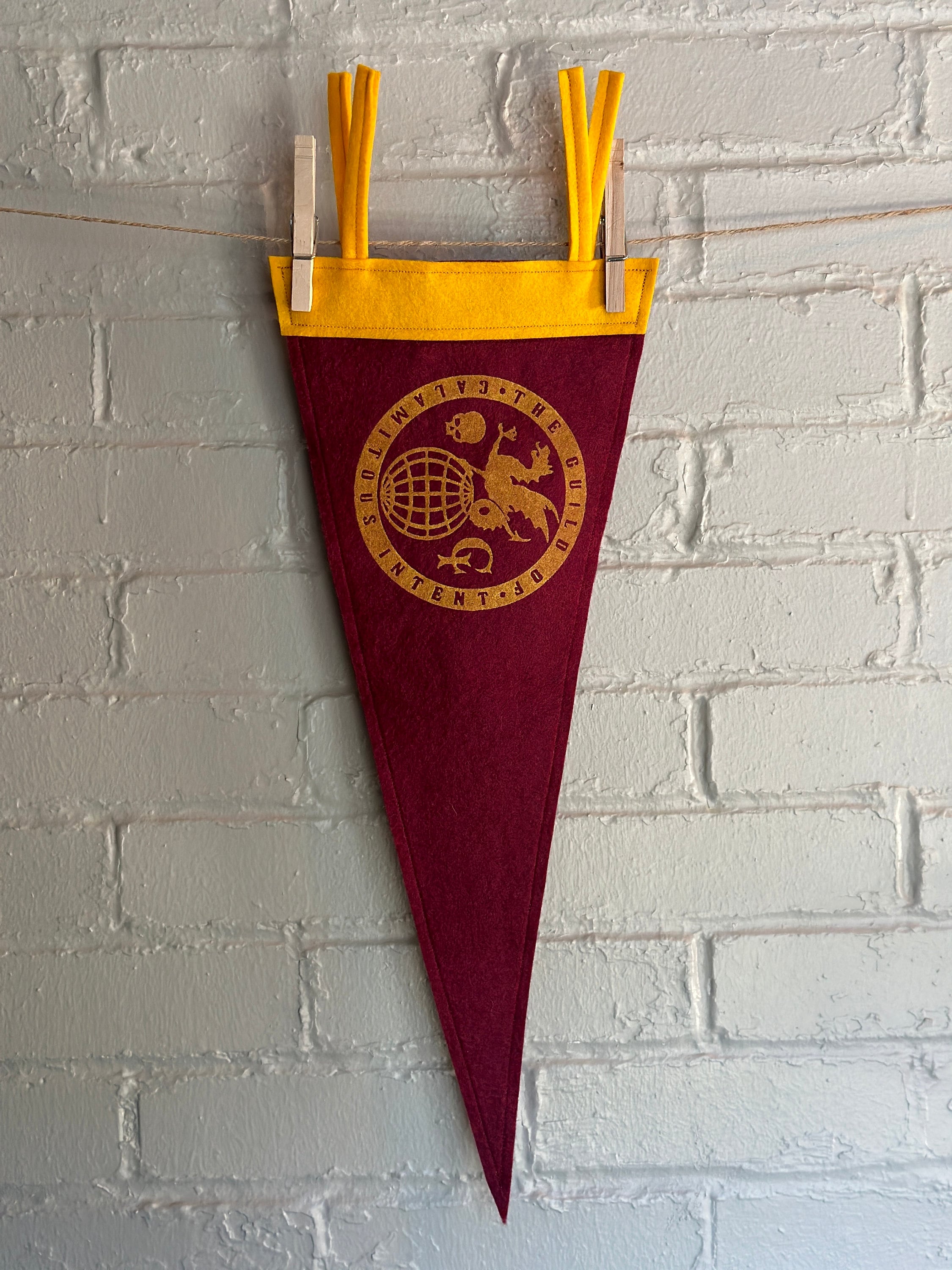 A burgundy pennant with yellow felt trim and the Guild of Calamitous Intent logo printed in yellow ink