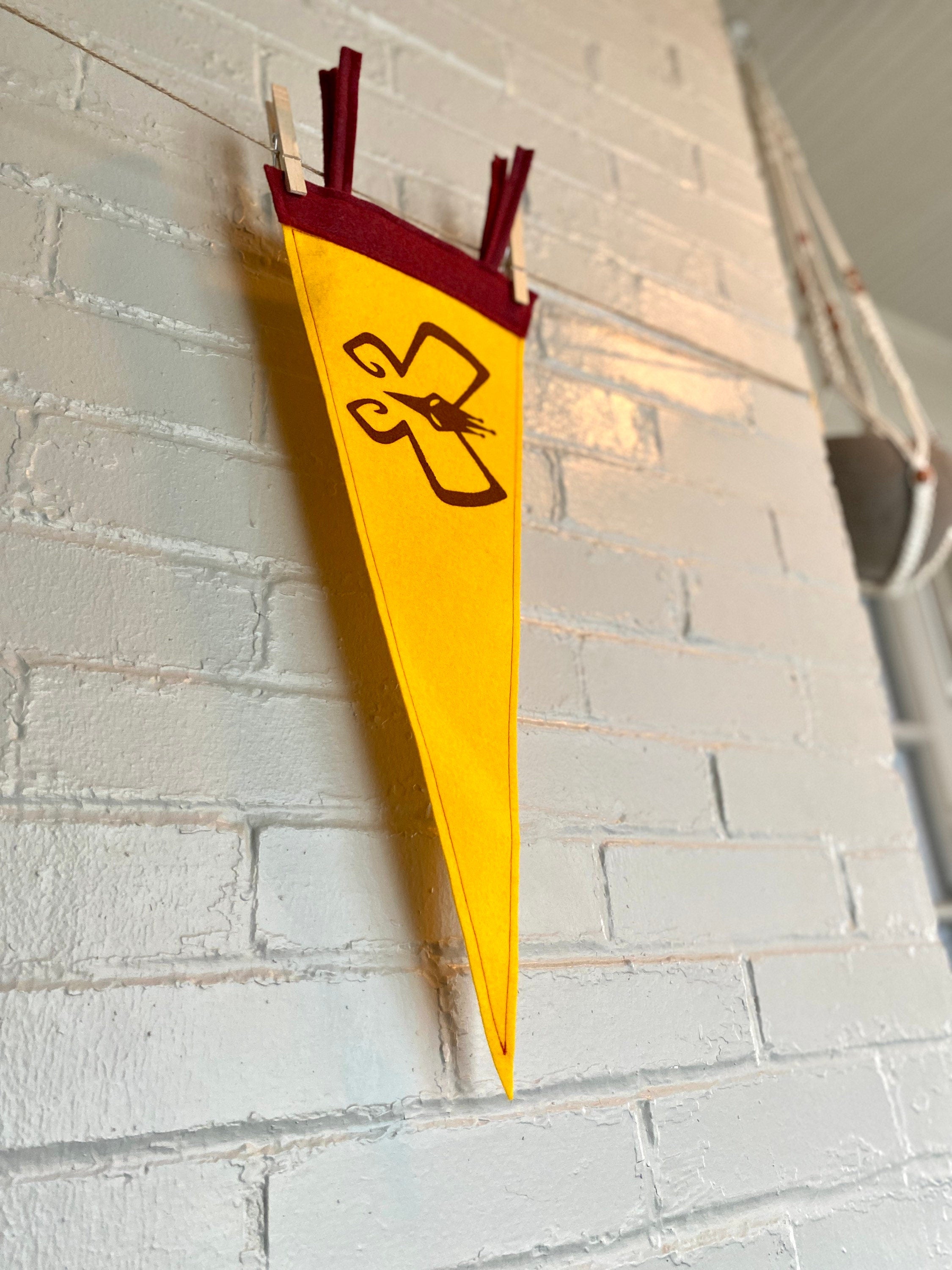 Side view of a yellow pennant with burgundy trim and the Monarch's insignia from the Venture Bros printed in burgundy ink