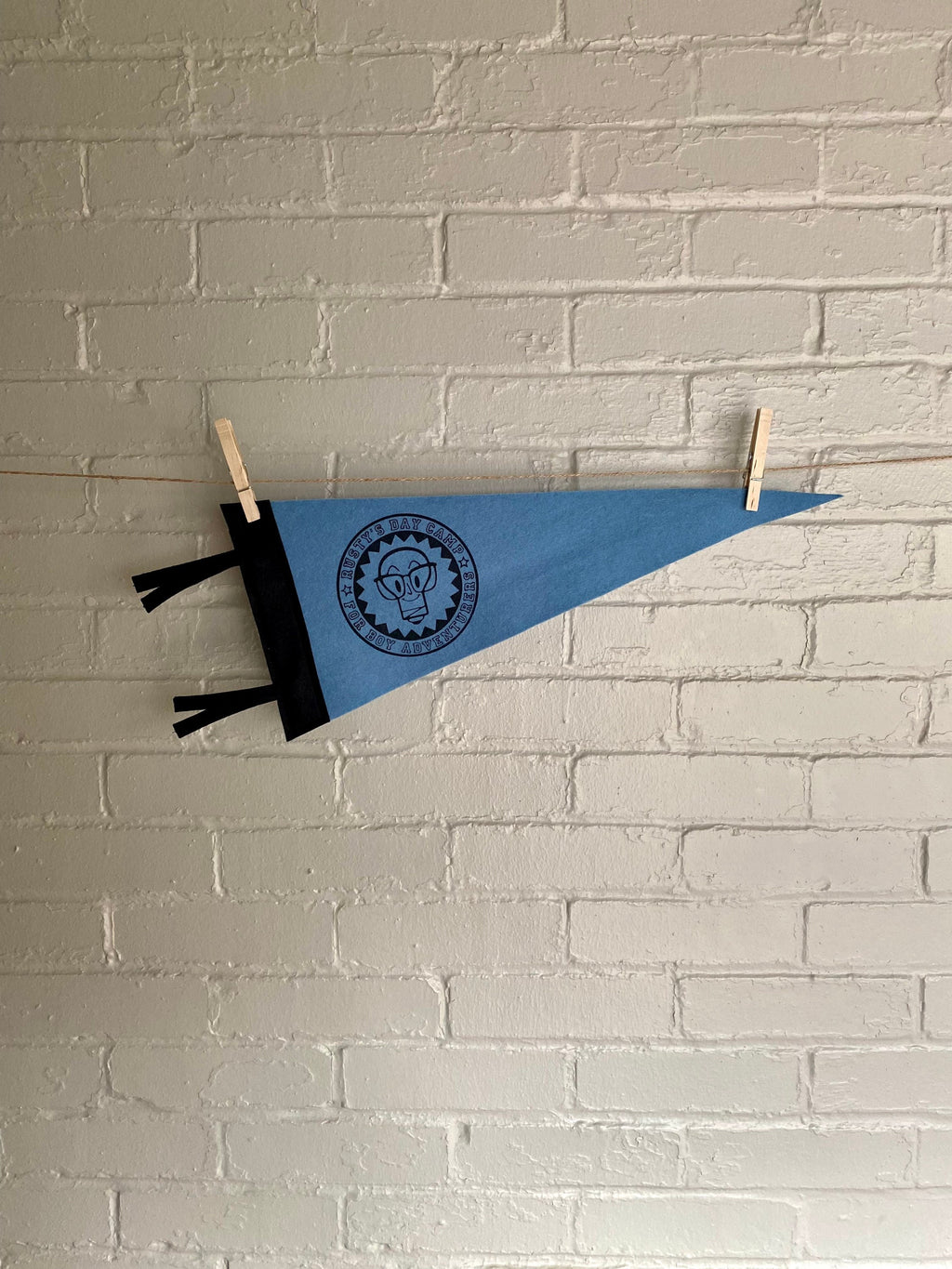 A sky blue felt pennant with black trim and a logo for "Rusty's Day Camp for Boy Adventurers" printed in black ink