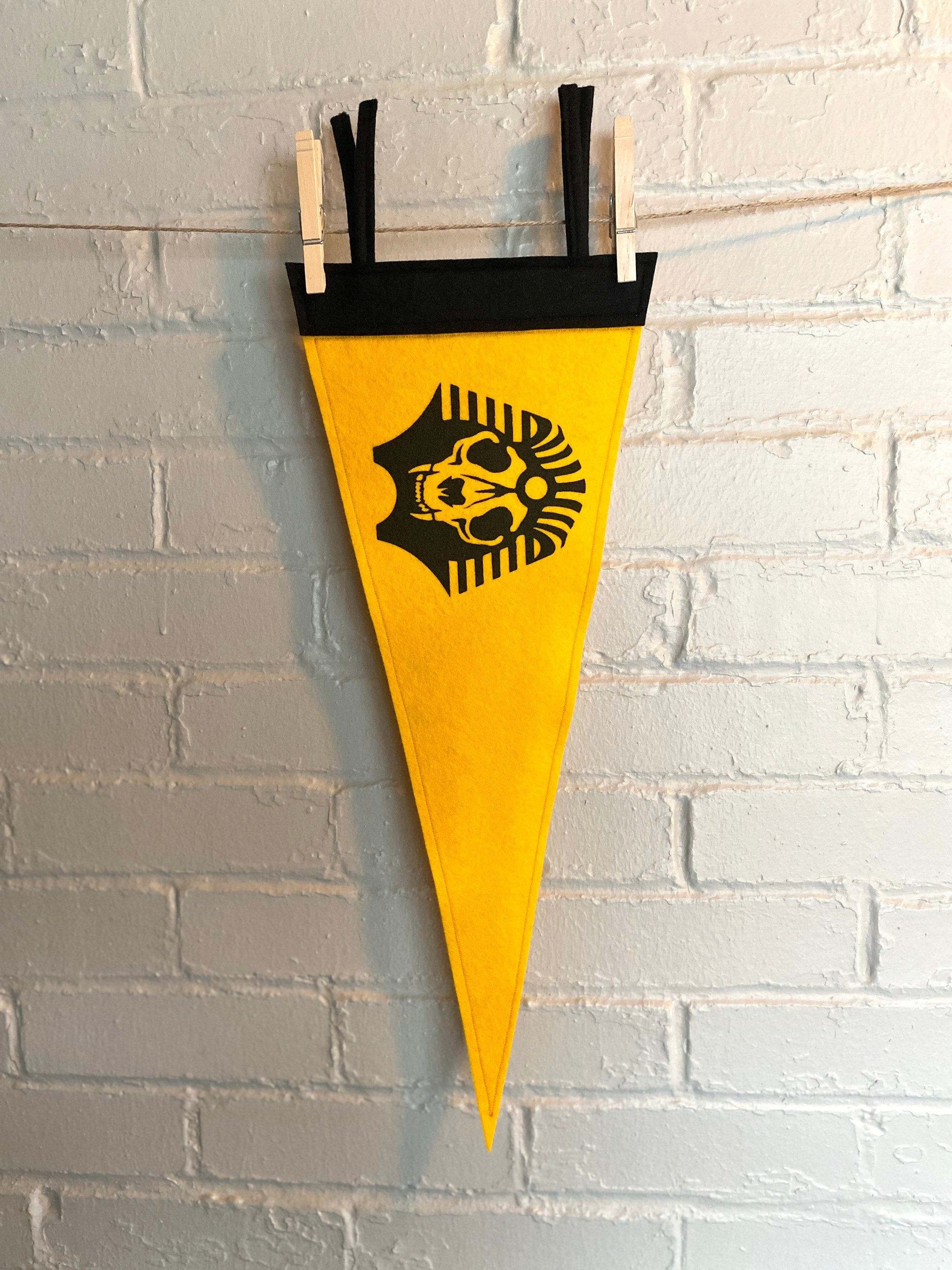A yellow felt pennant with black trim and the SPHINX logo from The Venture Bros cartoon printed in black ink