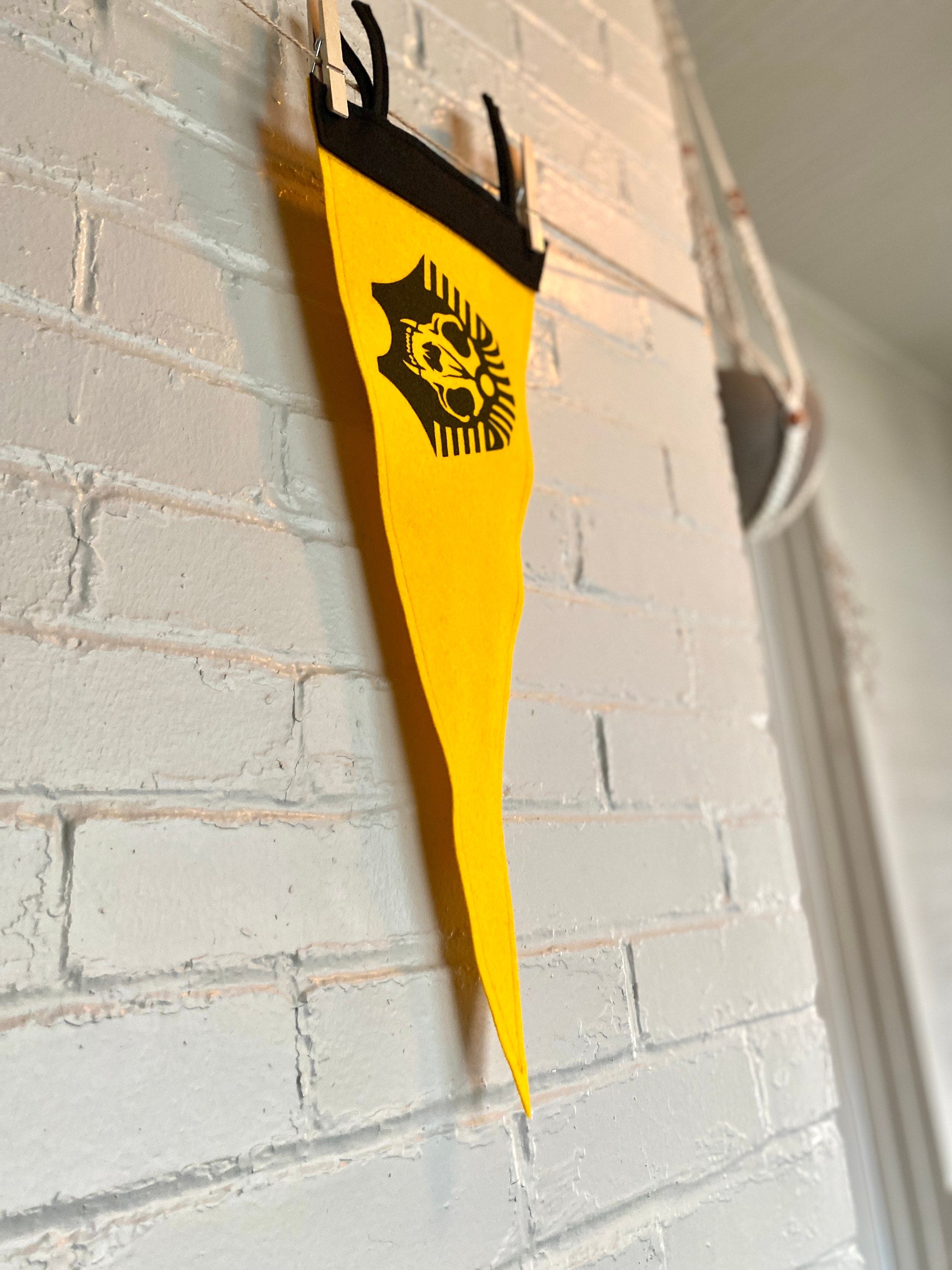 Side view of a yellow felt pennant with black trim and the SPHINX logo from The Venture Bros cartoon printed in black ink
