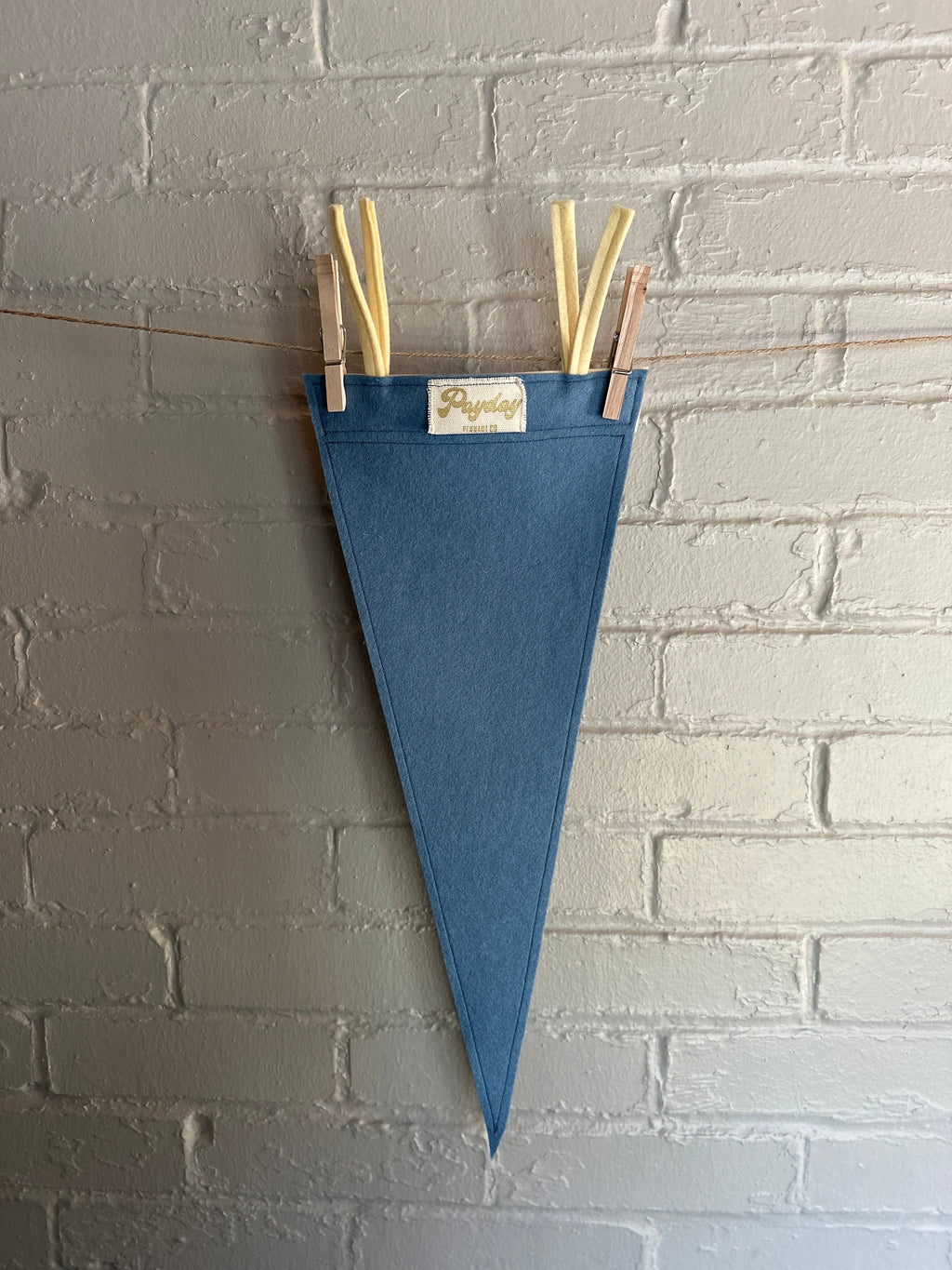 Back of a light blue felt pennant with cream trim and the Venture Bros logo printed on in white ink