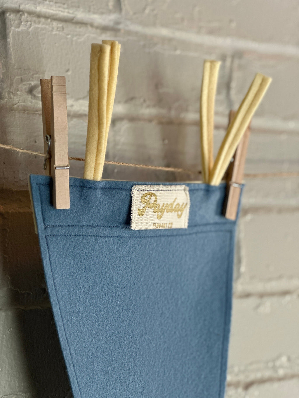 Closeup view of the tag on a light blue felt pennant with cream trim and the Venture Bros logo printed on in white ink