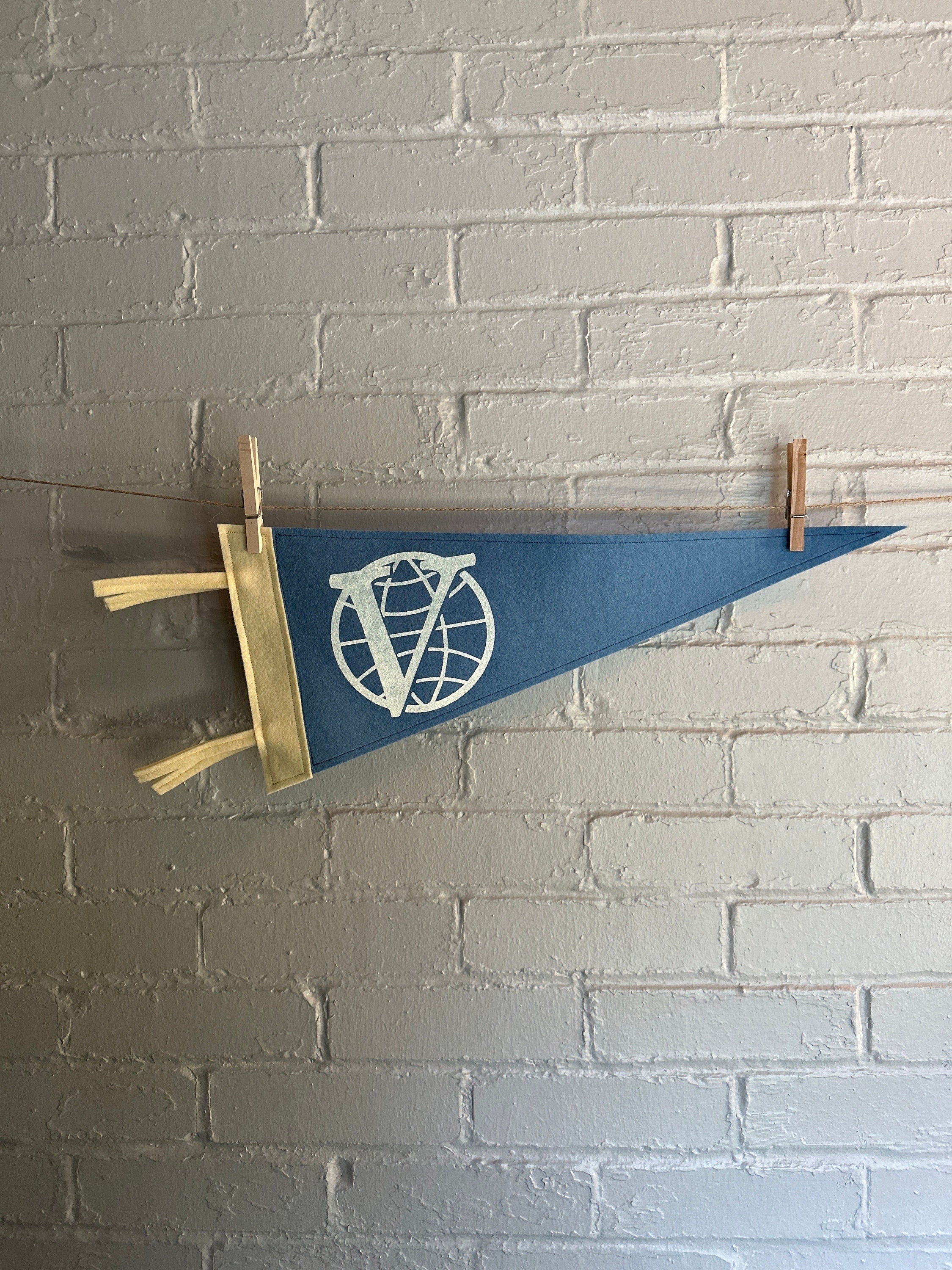 A light blue felt pennant with cream trim and the Venture Bros logo printed on in white ink
