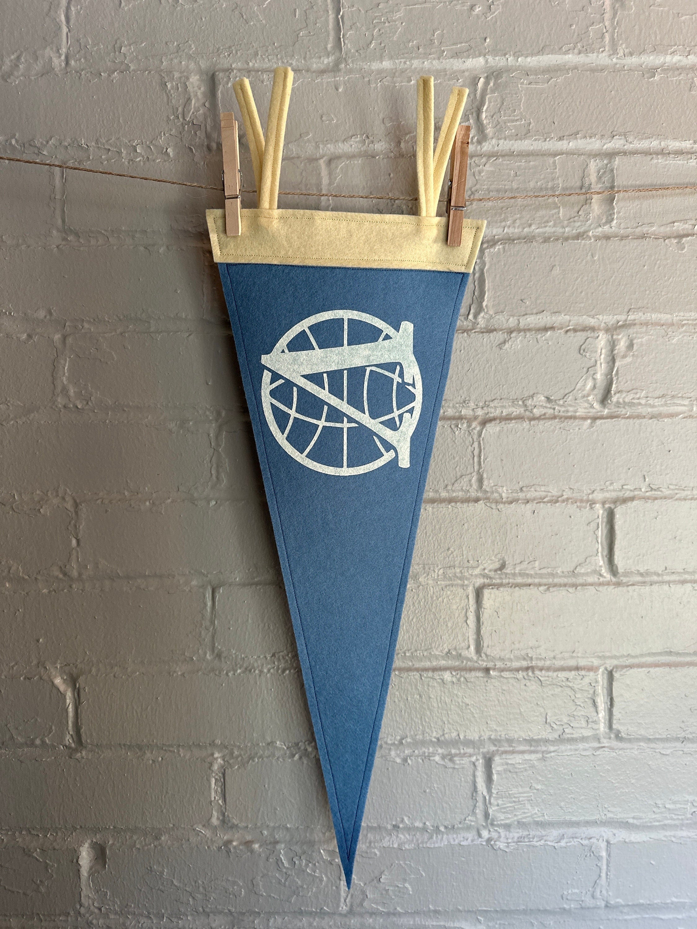 A light blue felt pennant with cream trim and the Venture Bros logo printed on in white ink