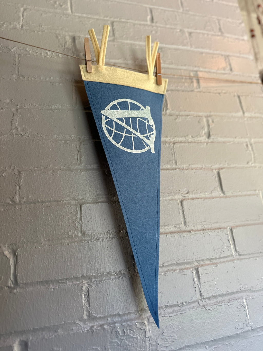 Side view of a light blue felt pennant with cream trim and the Venture Bros logo printed on in white ink