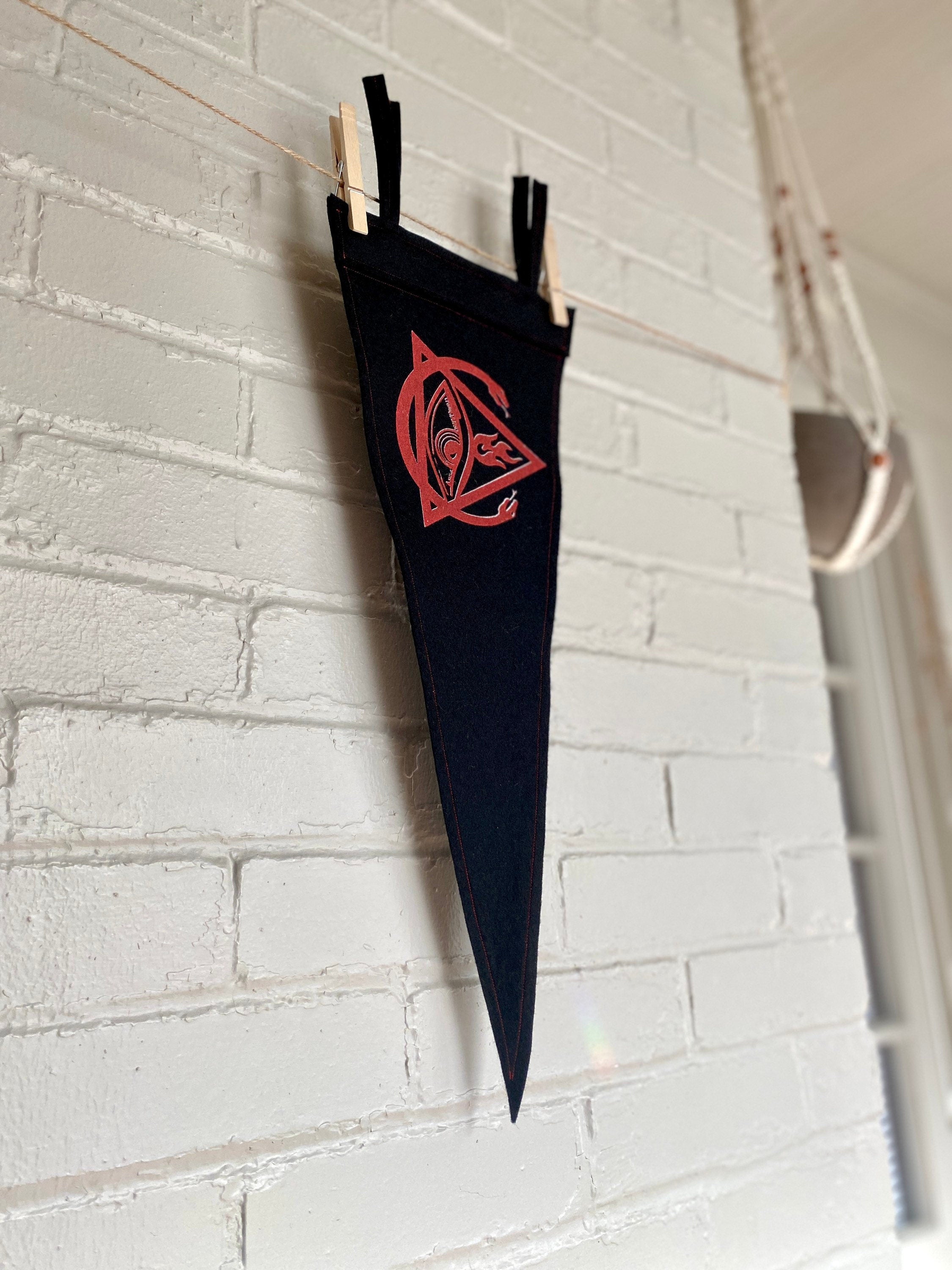 Side view of a black felt pennant with black trim and the Order of the Triad logo from The Venture Bros cartoon printed in red ink
