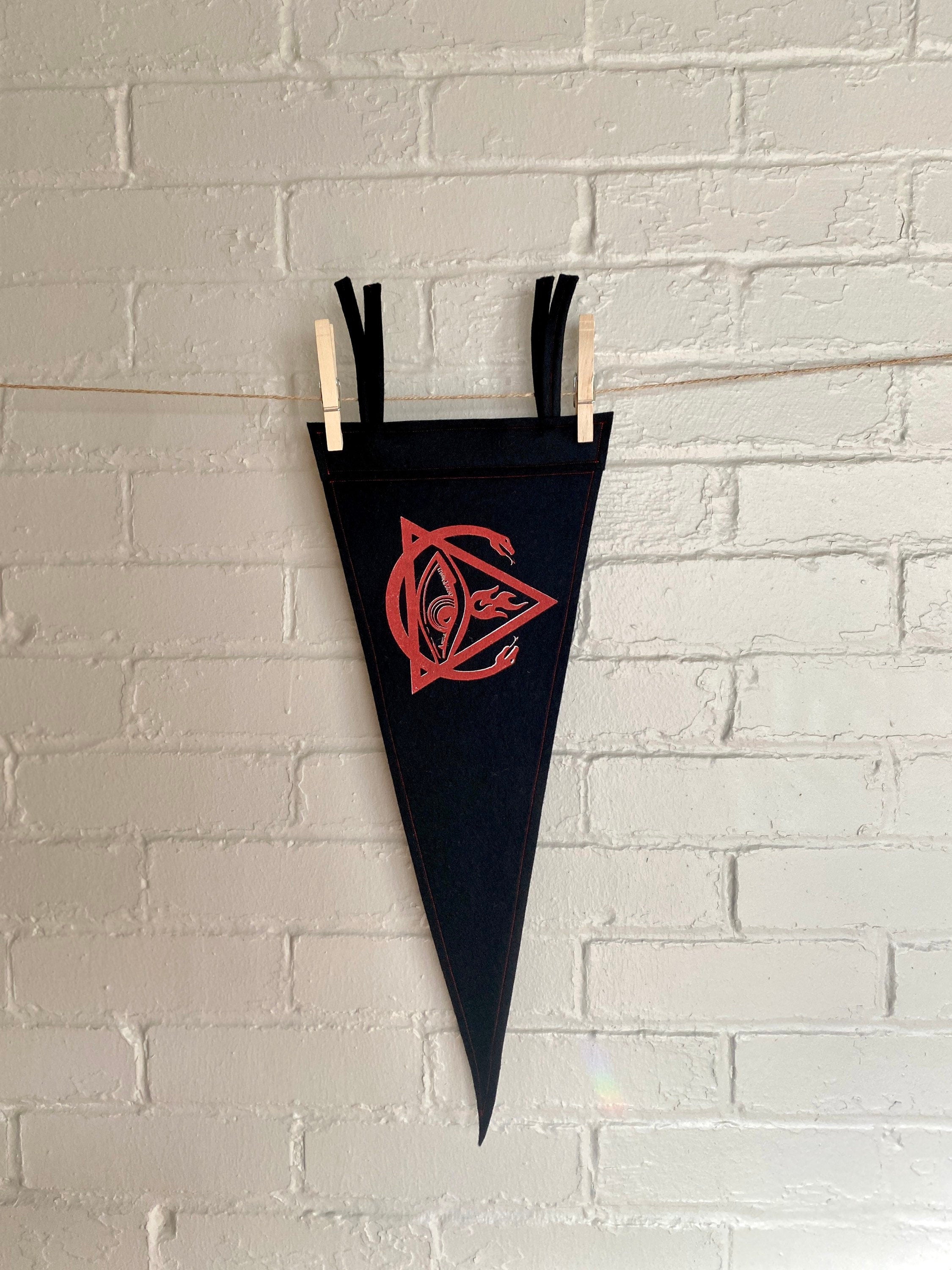 A black felt pennant with black trim and the Order of the Triad logo from The Venture Bros cartoon printed in red ink